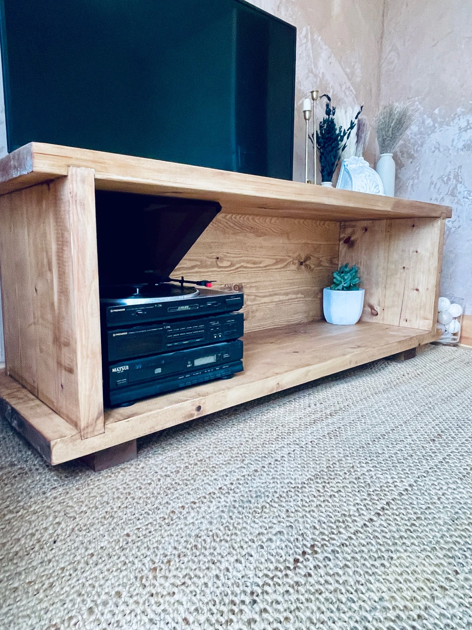 Chunky wooden TV console with open shelf housing record player and media equipment, natural finish