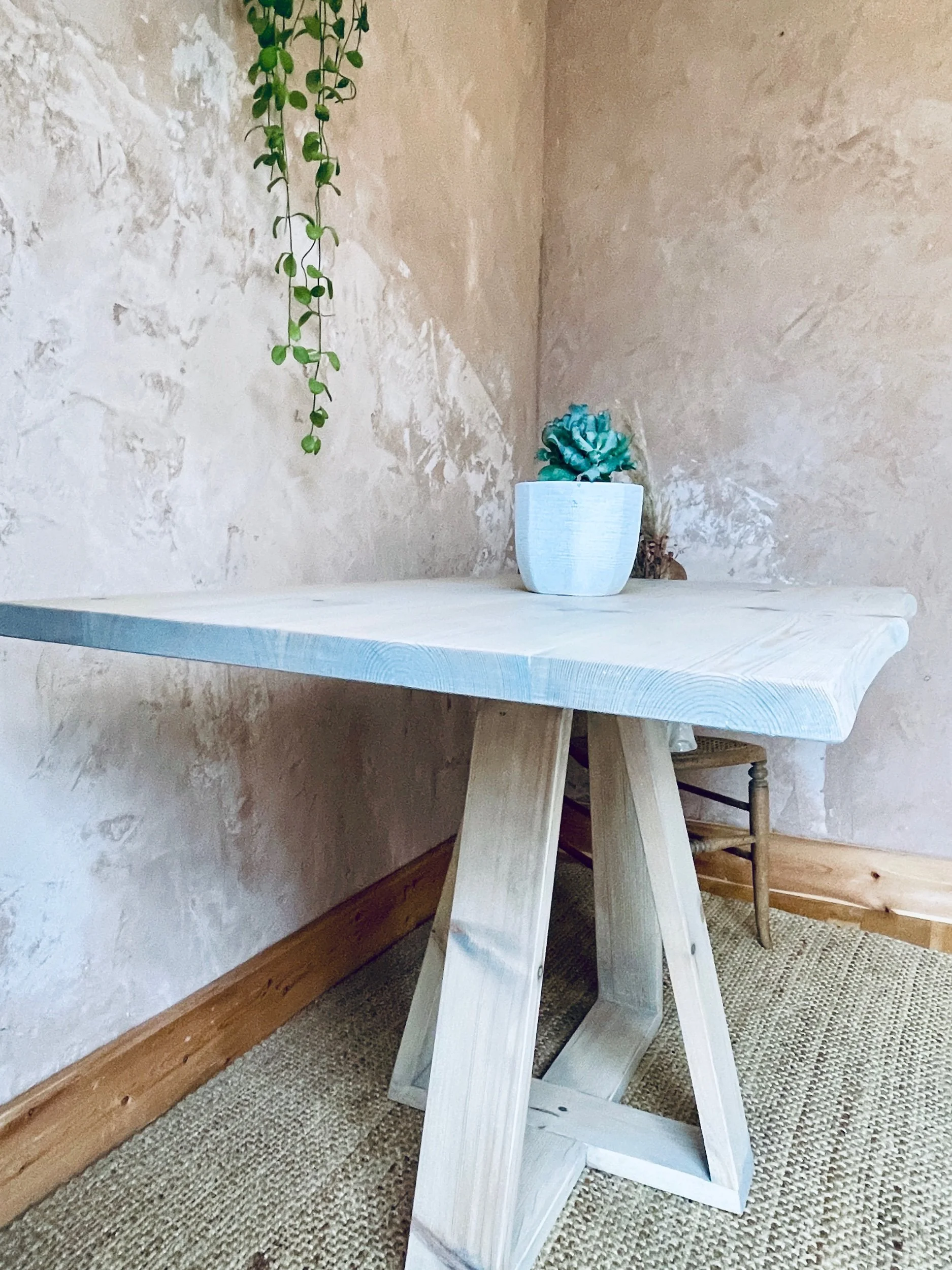 Side angle of light wooden dining table with tapered legs and small plant decoration.