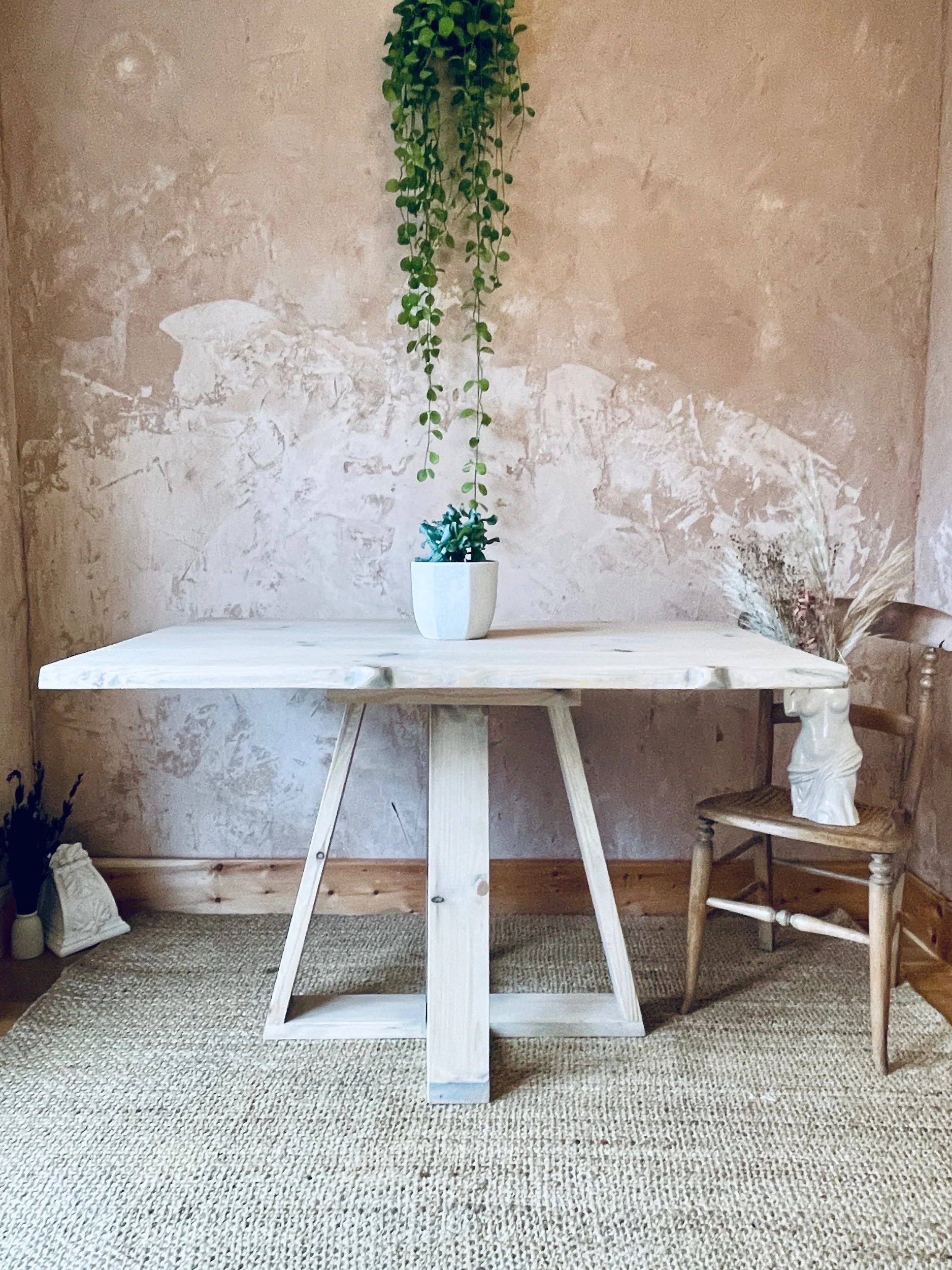 Light solid-wood dining table with tapered legs against plaster wall and hanging plant