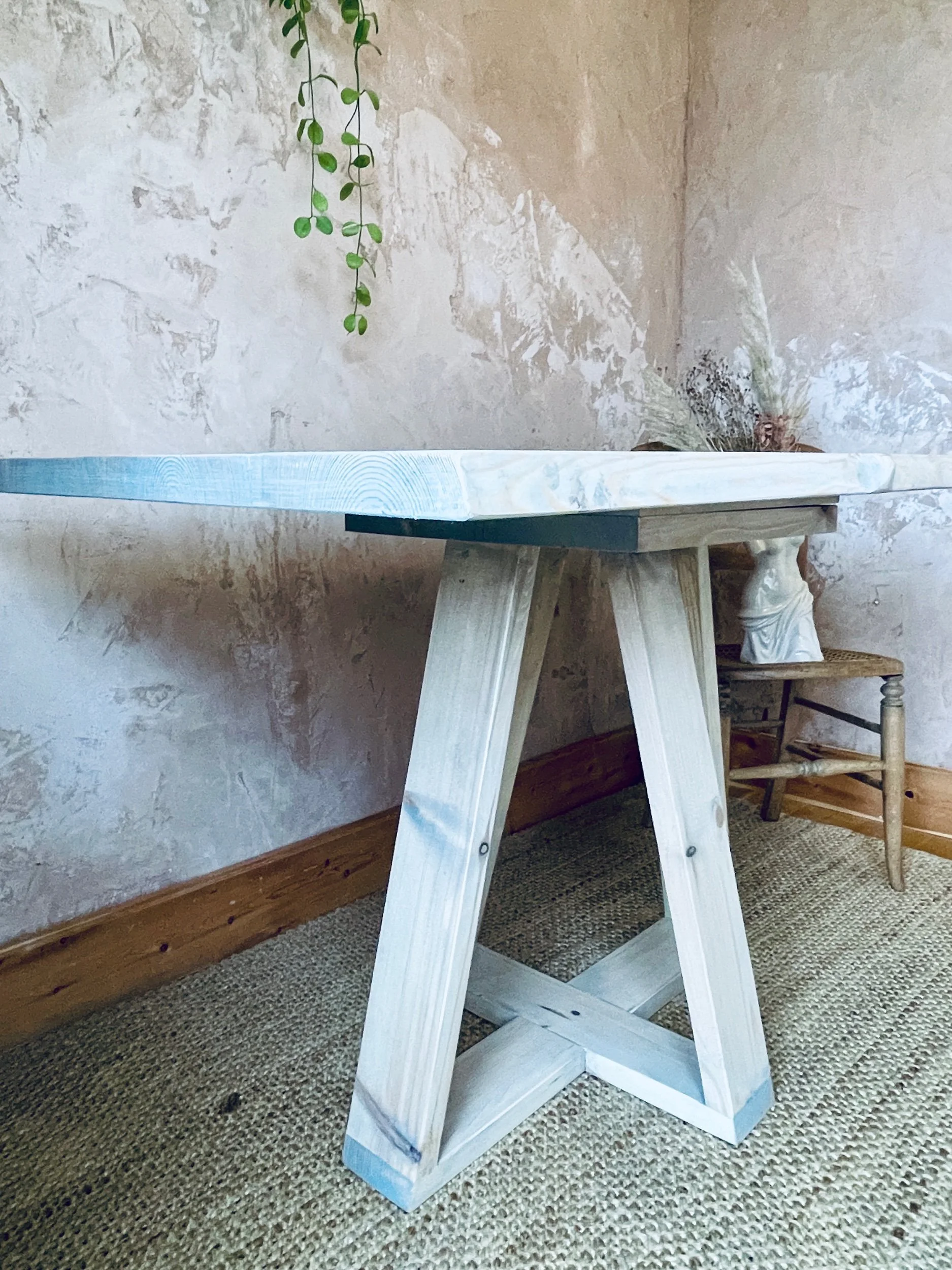 Side view of wooden dining table showing tapered leg detail and plant backdrop