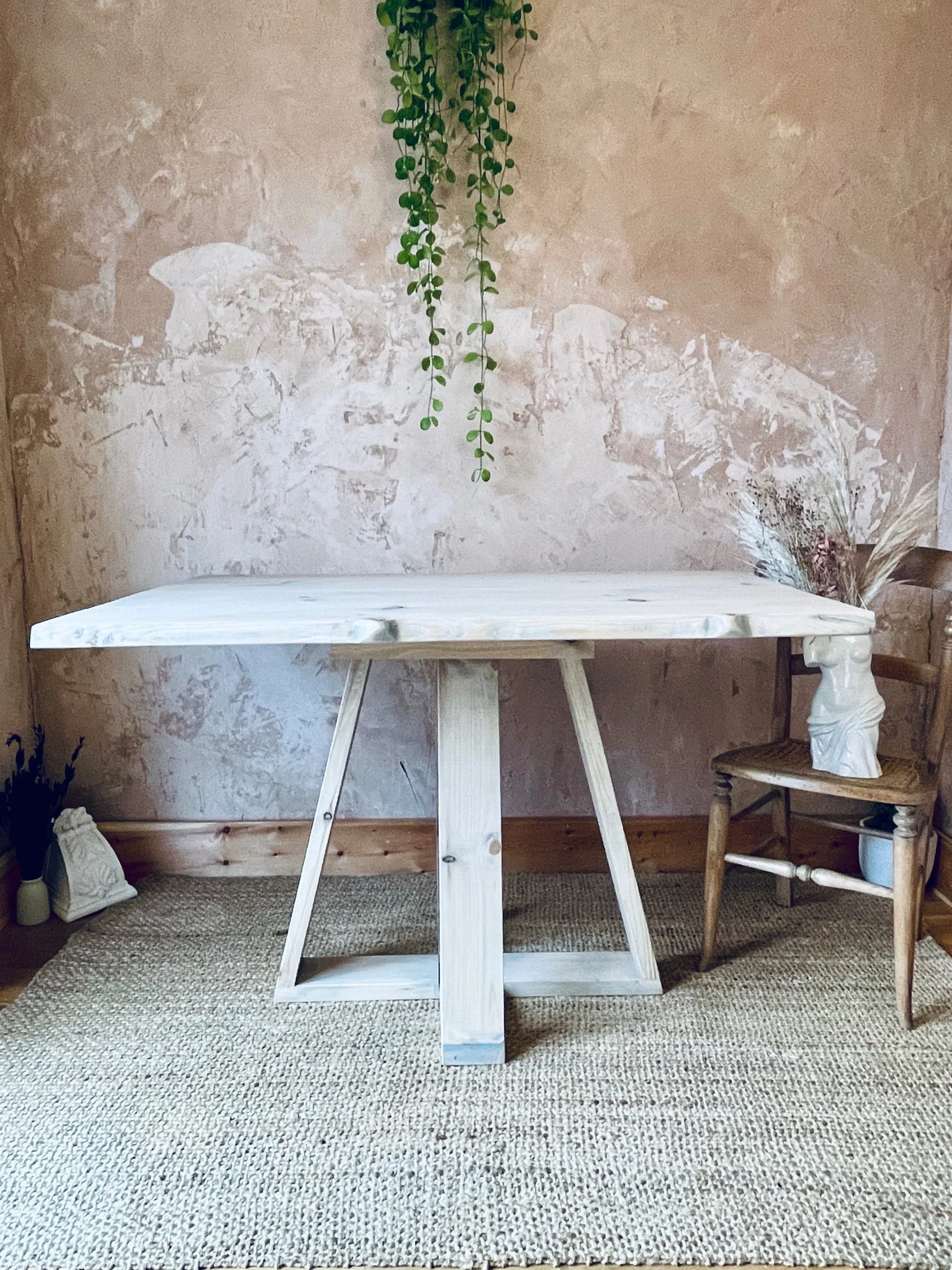 Front view of light solid-wood dining table with tapered legs and hanging plant backdrop