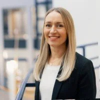 Nuori nainen hymyilee liiketilassa, taustalla suuria ikkunoita ja liiketilan sisätiloja.