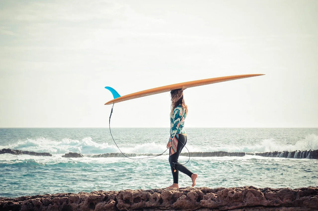 Surfer carrying a longboard along the rocks on a surf lesson near Ericeira