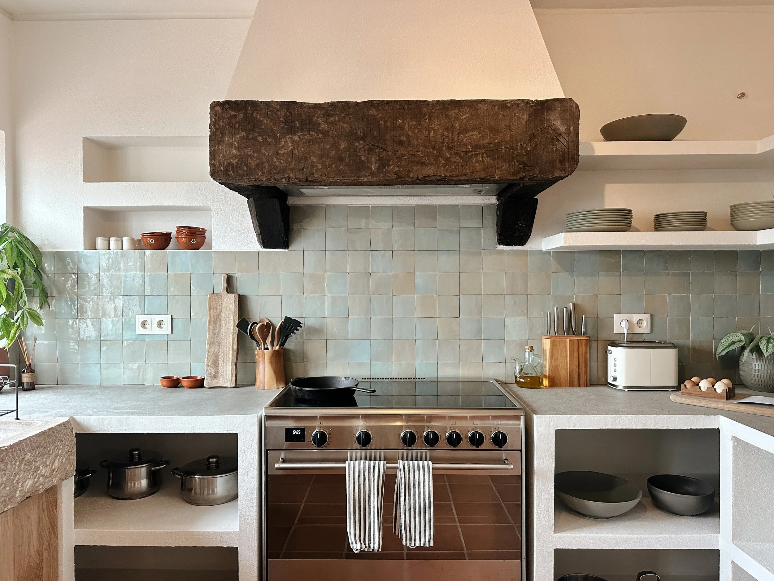 Living room with beige sofas, a wooden coffee table, potted plants, a fireplace, large window with white curtains, and wooden ceiling panels.