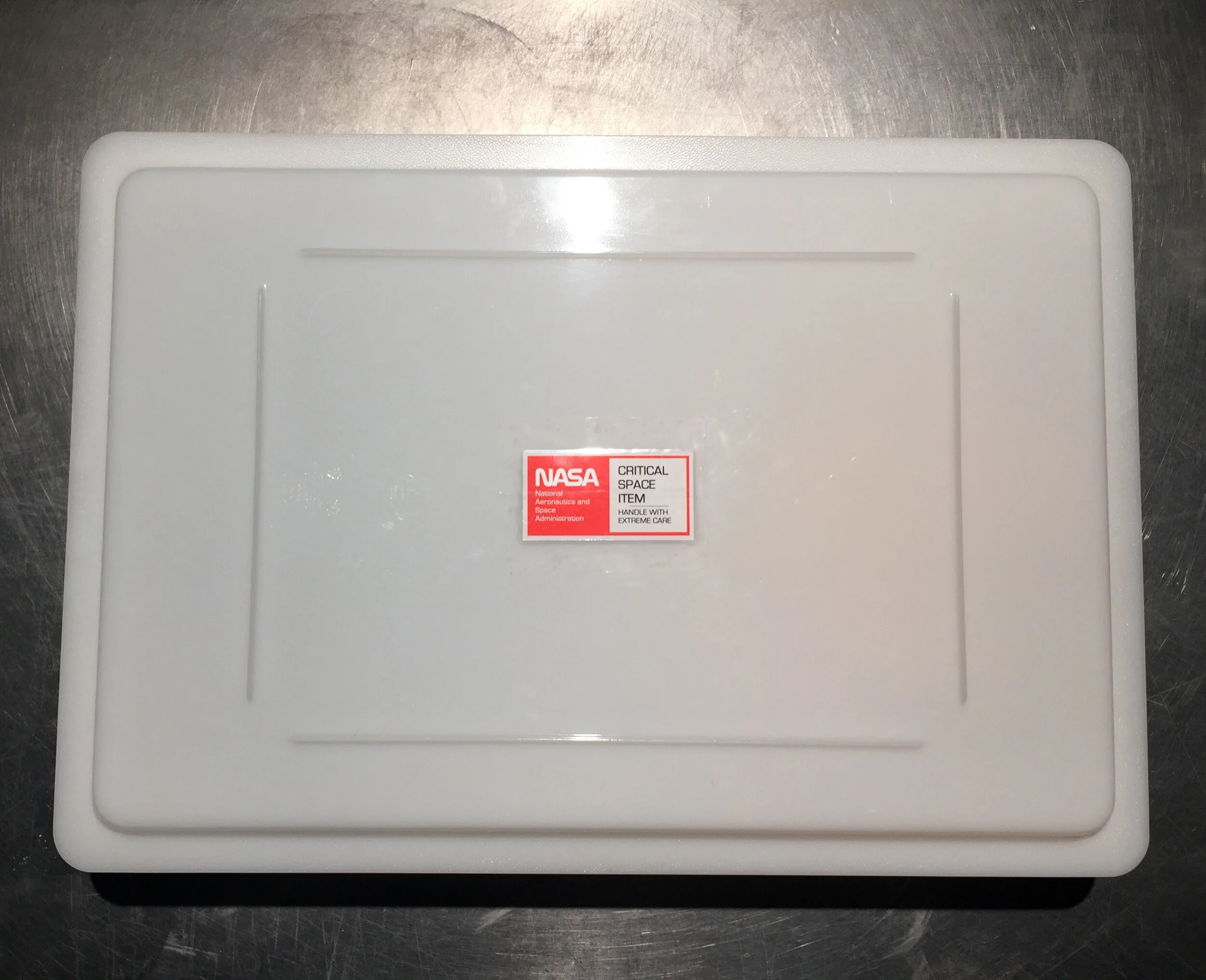 Michael Edward Miller Critical Space Item , 2018, dyed slip cast fired clay powder, laser cut coloured plexiglass, plastic catering container, authentic NASA critical space item label, altered authentic NASA non-disclosure agreements, respiratory masks, hypoallergenic gloves, stainless steel tables, plastic quarantine sheets, actors, participants