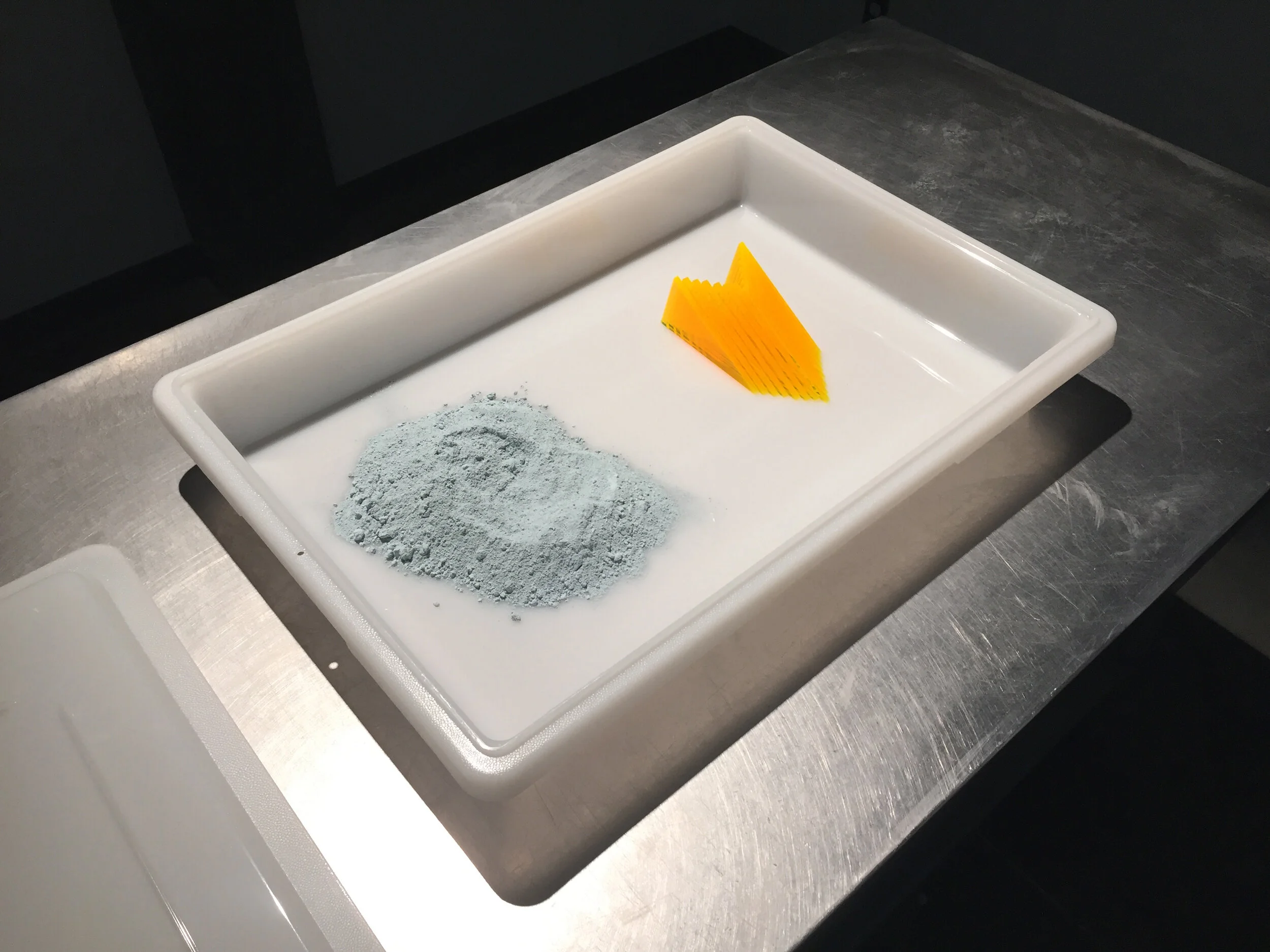 Michael Edward Miller Critical Space Item , 2018, dyed slip cast fired clay powder, laser cut coloured plexiglass, plastic catering container, authentic NASA critical space item label, altered authentic NASA non-disclosure agreements, respiratory masks, hypoallergenic gloves, stainless steel tables, plastic quarantine sheets, actors, participants