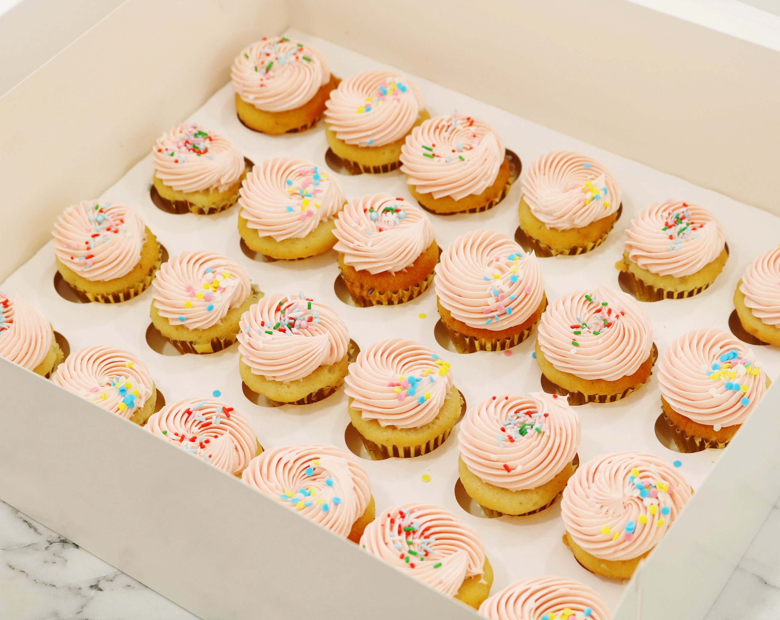 mini vanilla cupcakes for birthdays in pastel pink and rainbow sprinkles.
