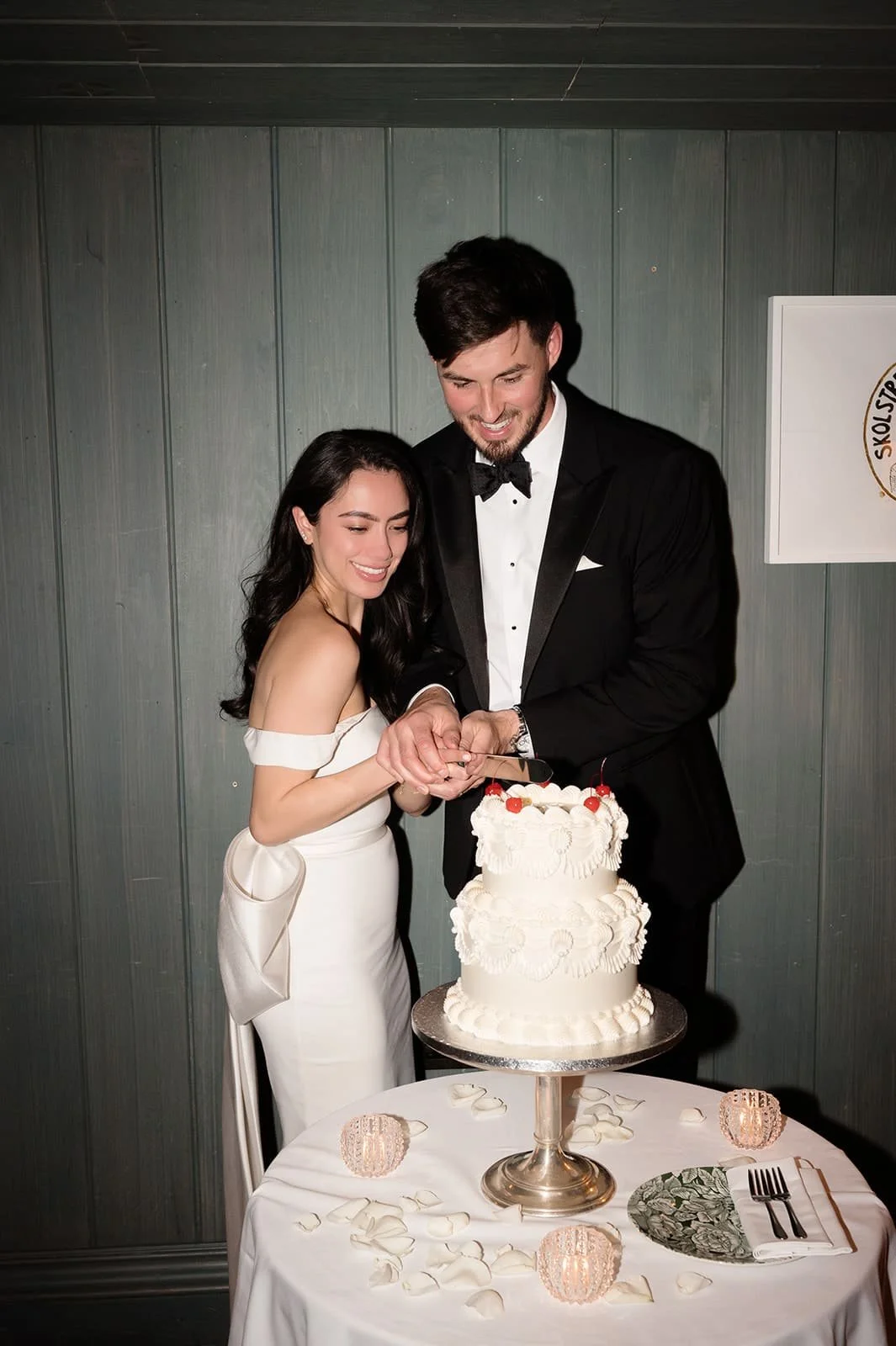 A woman in a wedding dress is blowing out candles on a wedding cake, while a man in a tuxedo helps her by holding a lit candle.