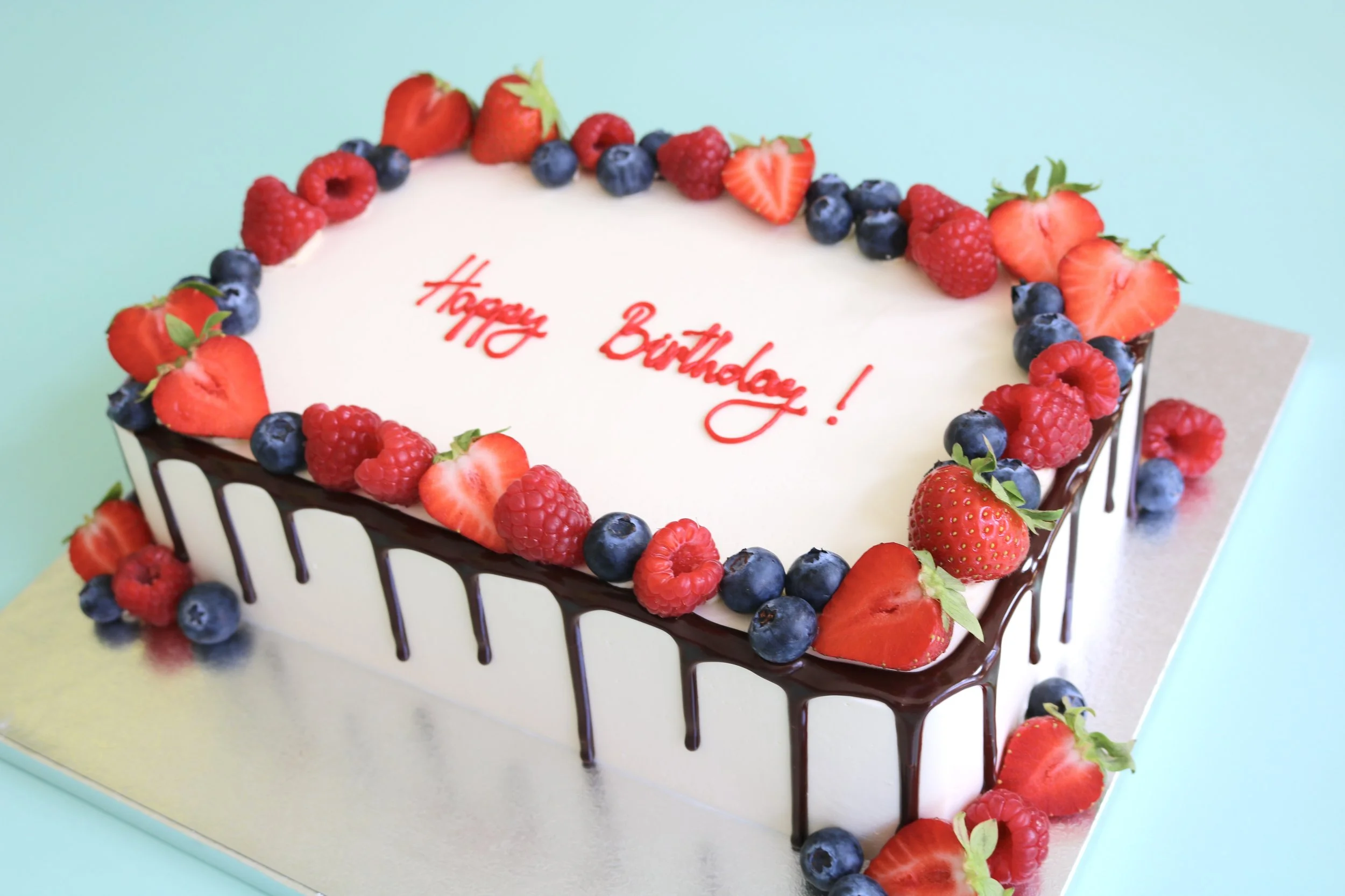 Rectangular birthday cake with fresh strawberries, raspberries, blueberries and chocolate drip decoration in London.