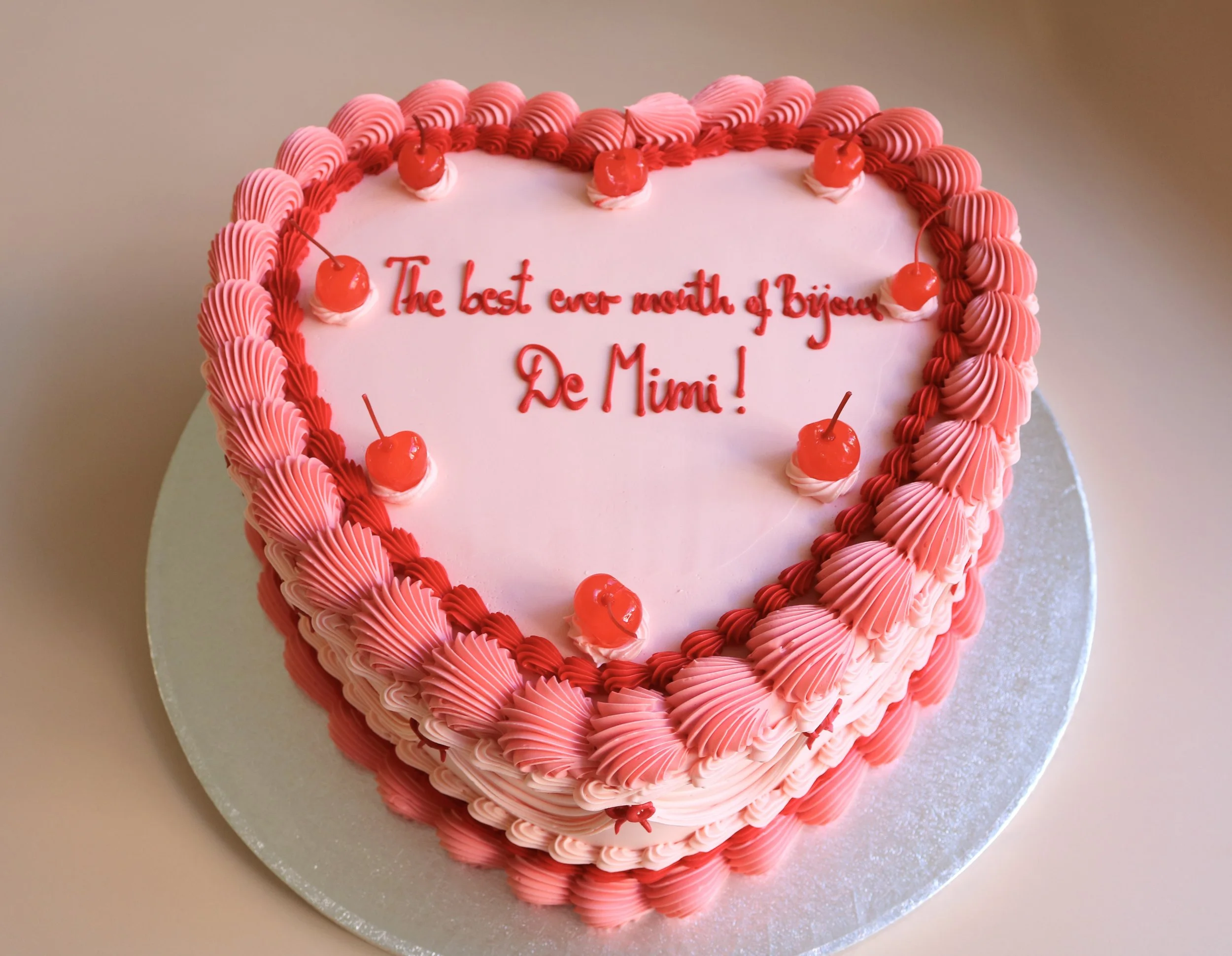 Vintage heart-shaped cake with red and pink buttercream piping, maraschino cherries, and red bows, ideal for corporate catering, office parties, and company celebrations.