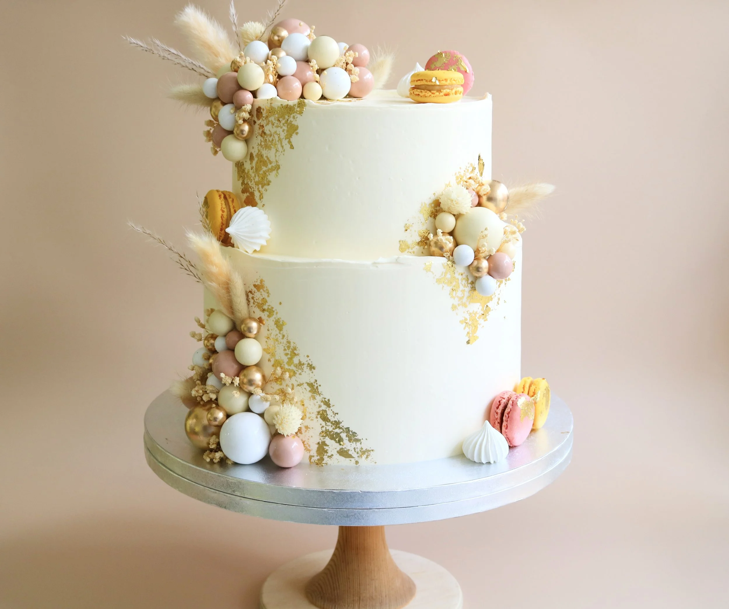 Two-tier birthday cake with blush and gold balloon decorations, dried flowers, macarons and edible gold leaf in London