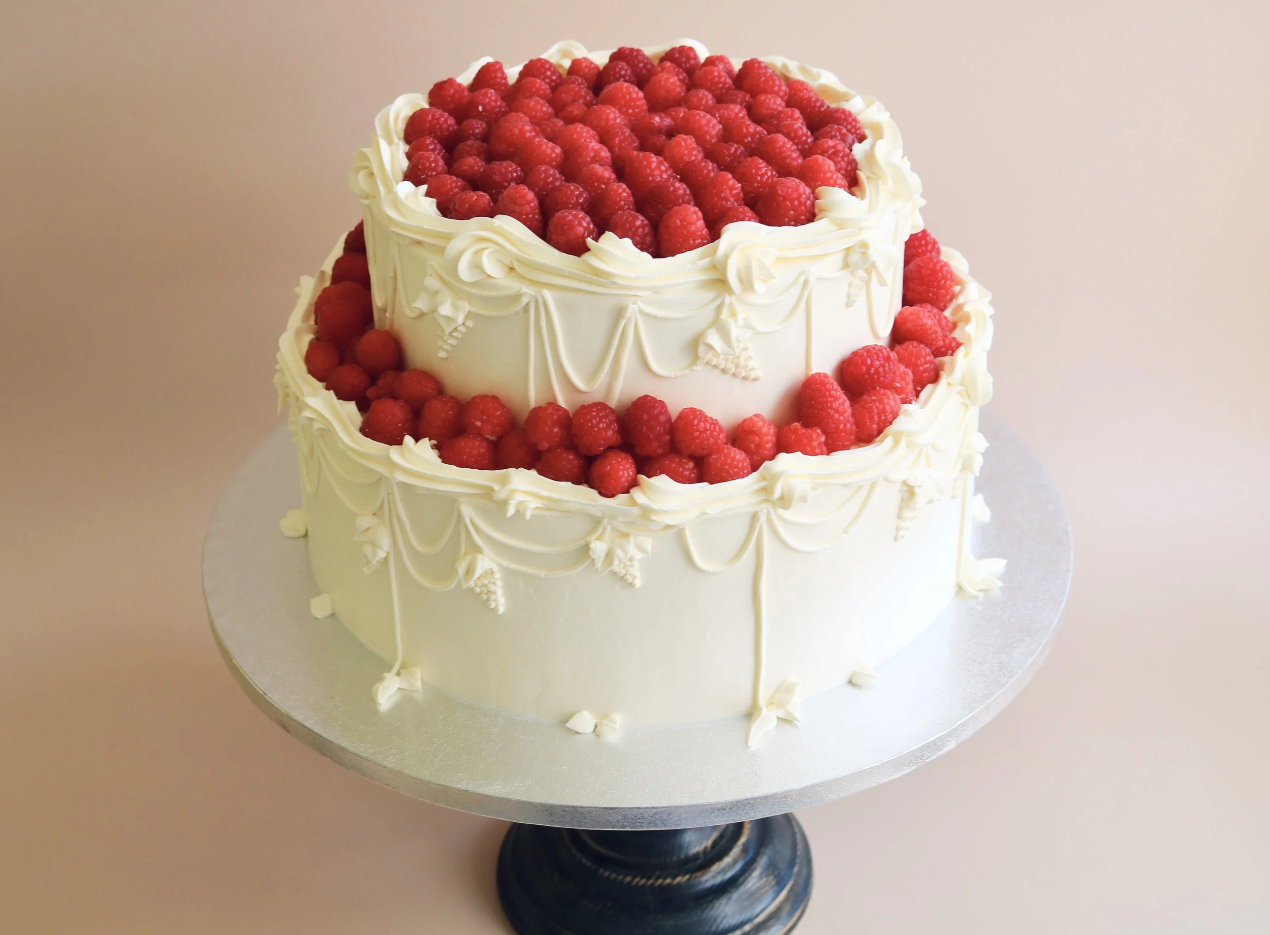 Two-tier raspberry wedding cake with intricate hand-piped grape clusters, delicate leaves and vintage buttercream swags.