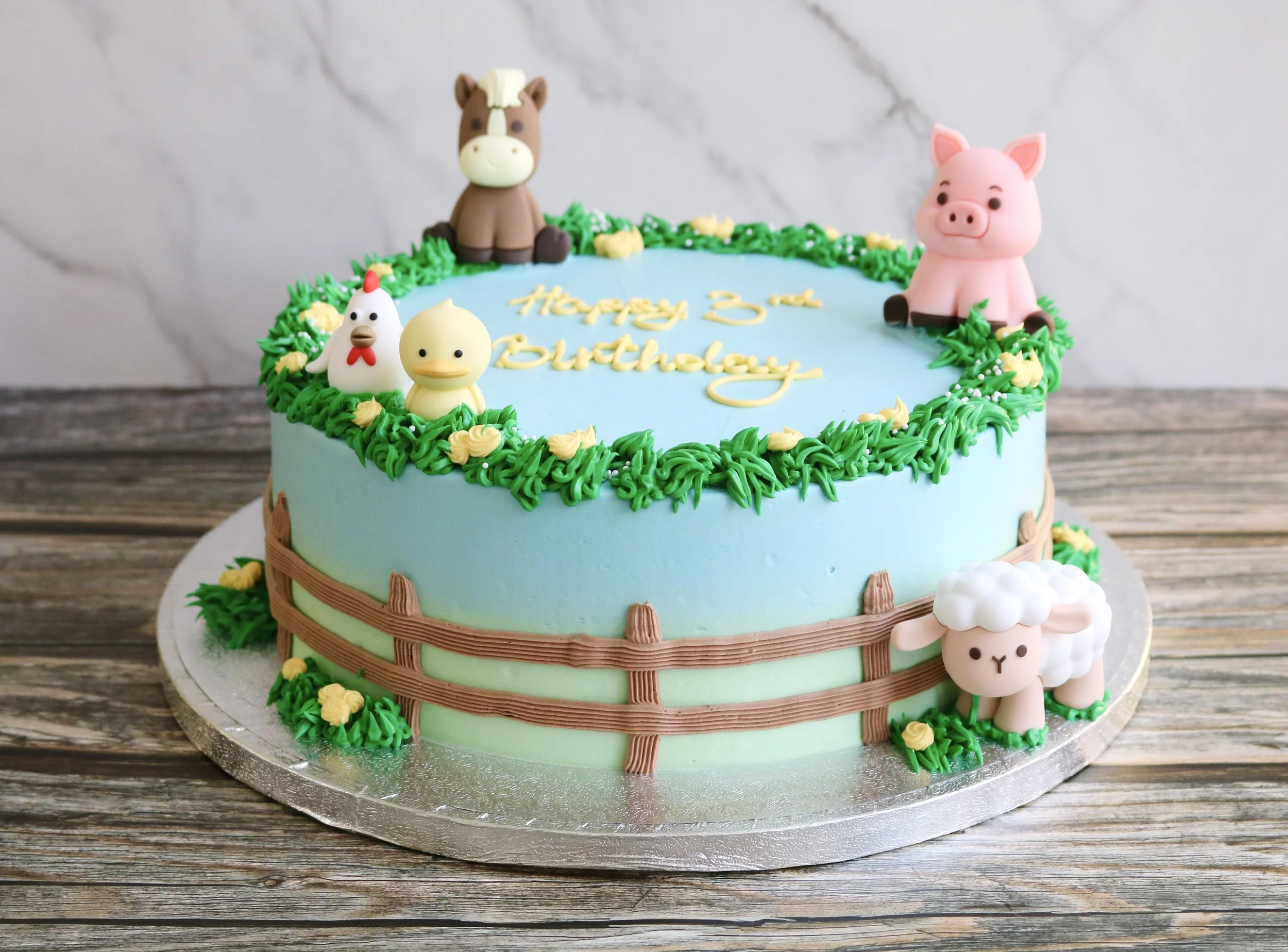 Pastel blue and green farm animal birthday cake with pig, horse, sheep, chick and hen toppers, piped grass and buttercream fence.