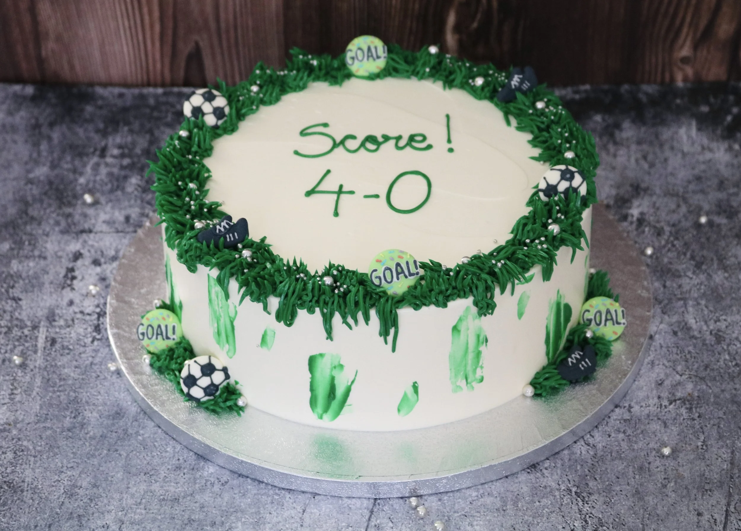 football birthday cake decorated with edible football toppers, green grasses and silver pearls around with a custom cake message on top