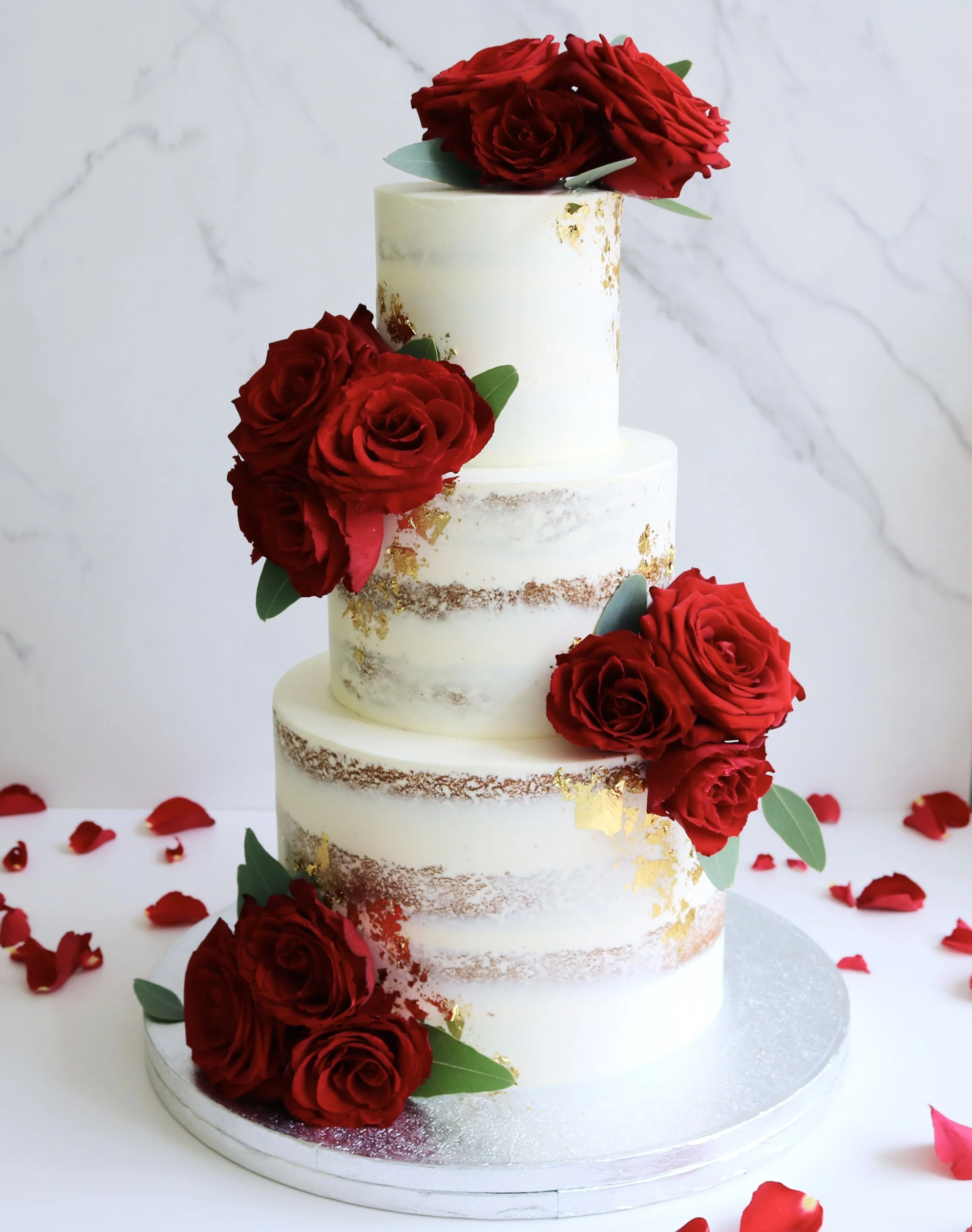 Semi-naked wedding cake with fresh red roses and edible gold leaf, available in one to three tiers