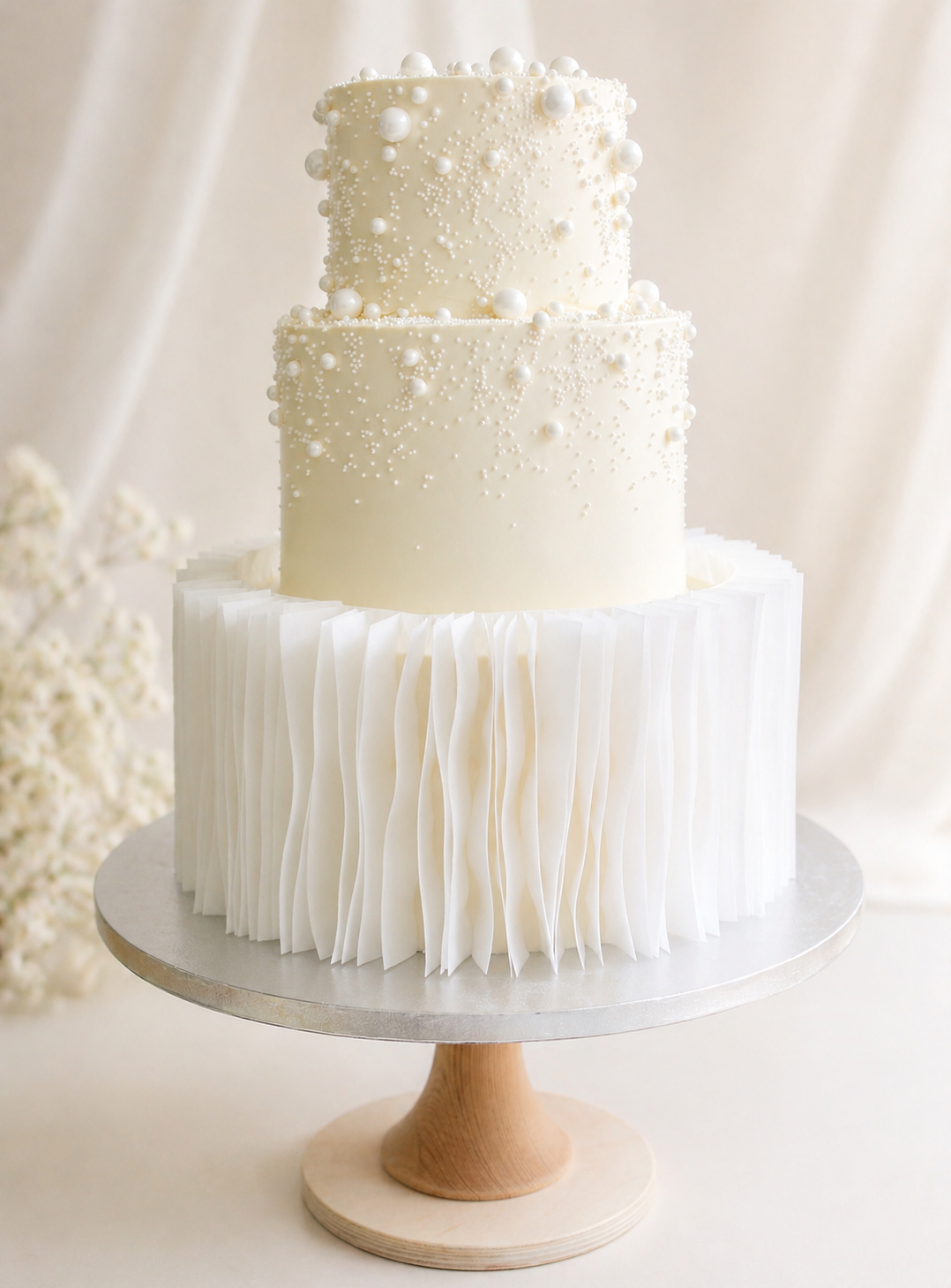 Luxury wedding cake in London with cream finish, edible wafer paper ruffles, cascading edible pearls, and optional Gypsophila styling. Available in 3-tier sizes.