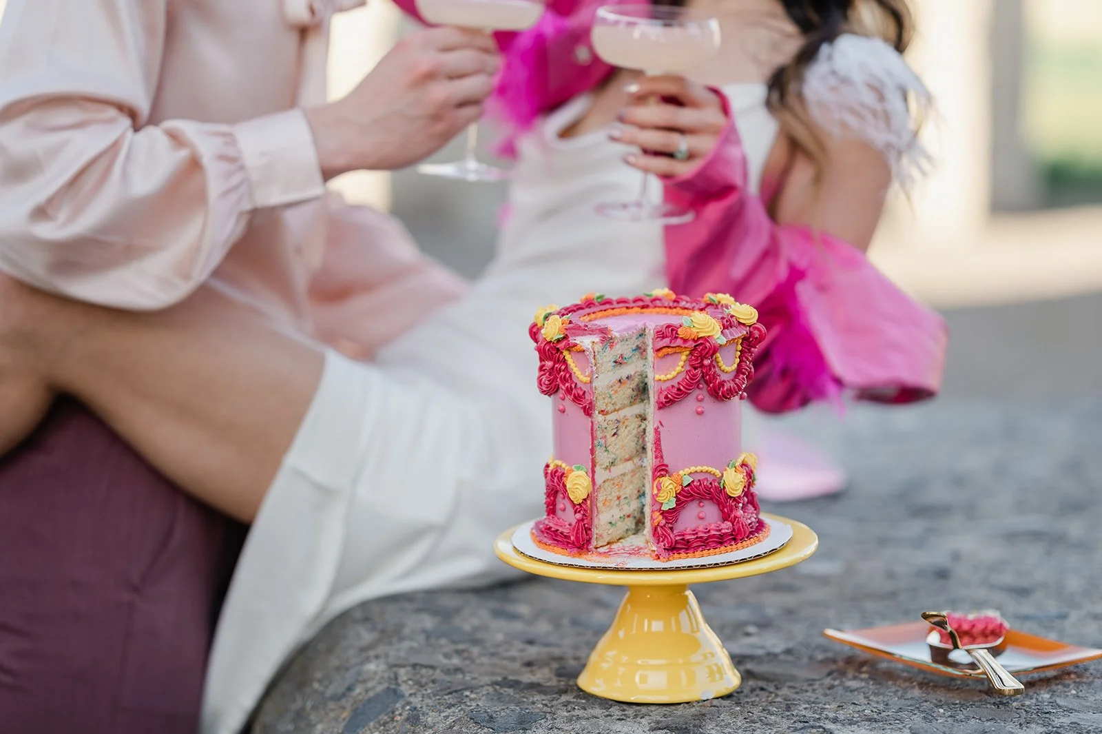 colorful wedding cake with the couple drinking champagne in the background