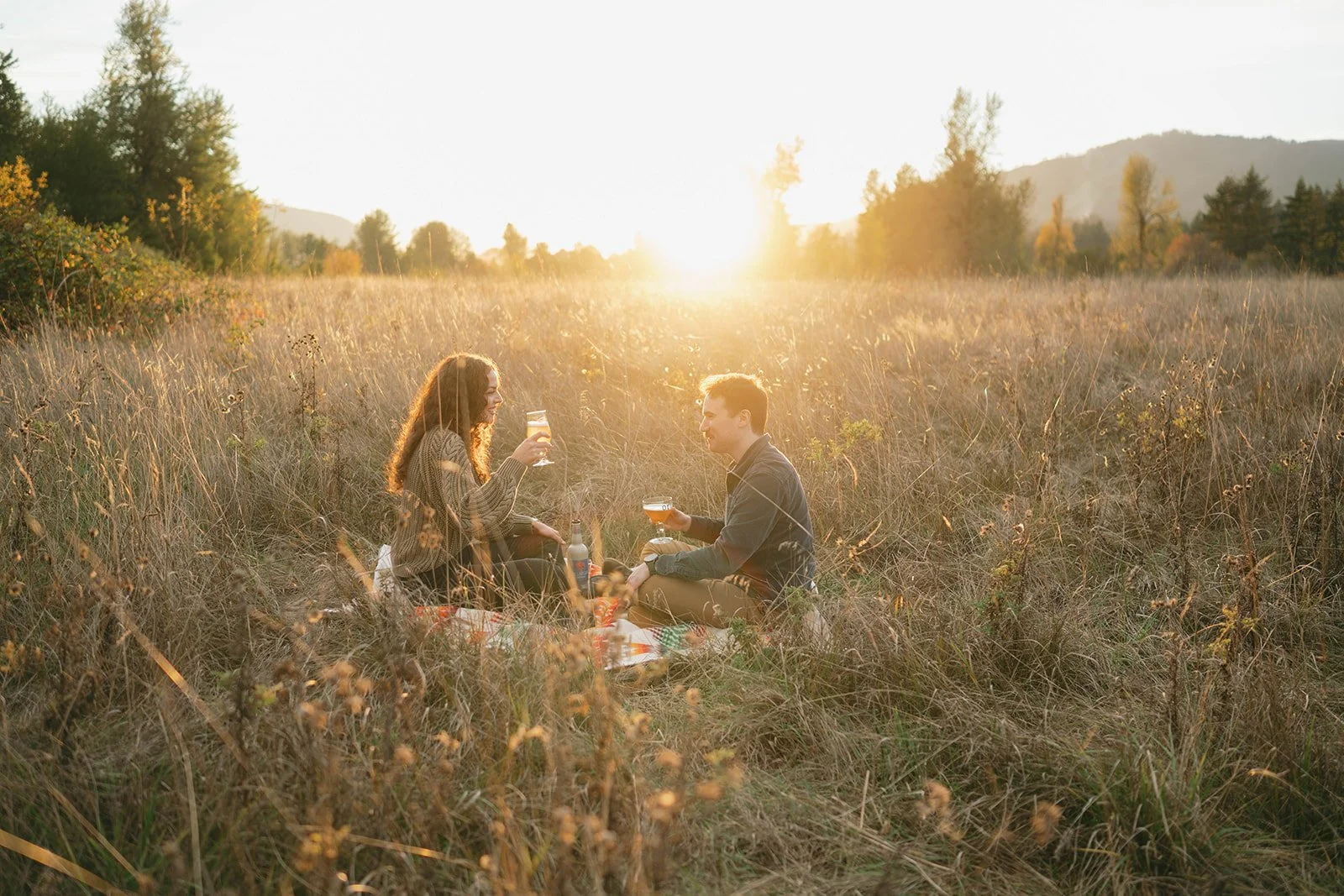 recently engaged couple sitting in a grass field drinking beers