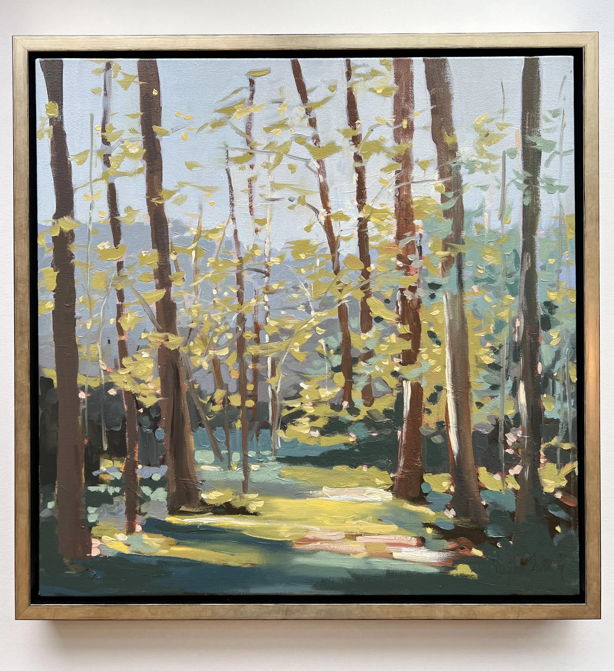 Original oil landscape painting by Asheville artist Cheyenne Trunnell depicting soft light illuminating a forest path and distant mountains, framed in champagne, 24×24 inches.