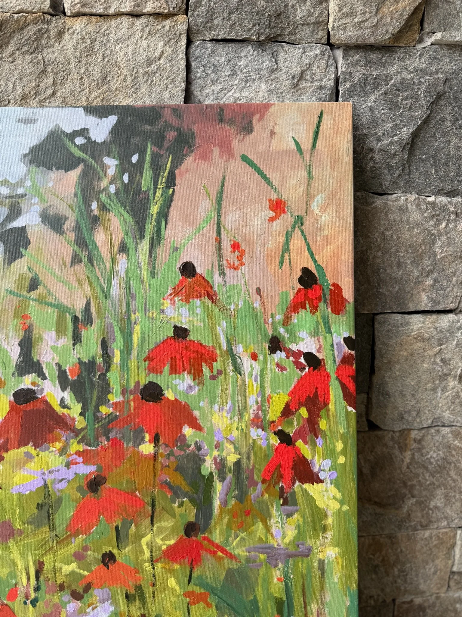 Original mixed media wildflower painting by Cheyenne Trunnell displayed against a stone wall, featuring red-orange blooms and layered green foliage.