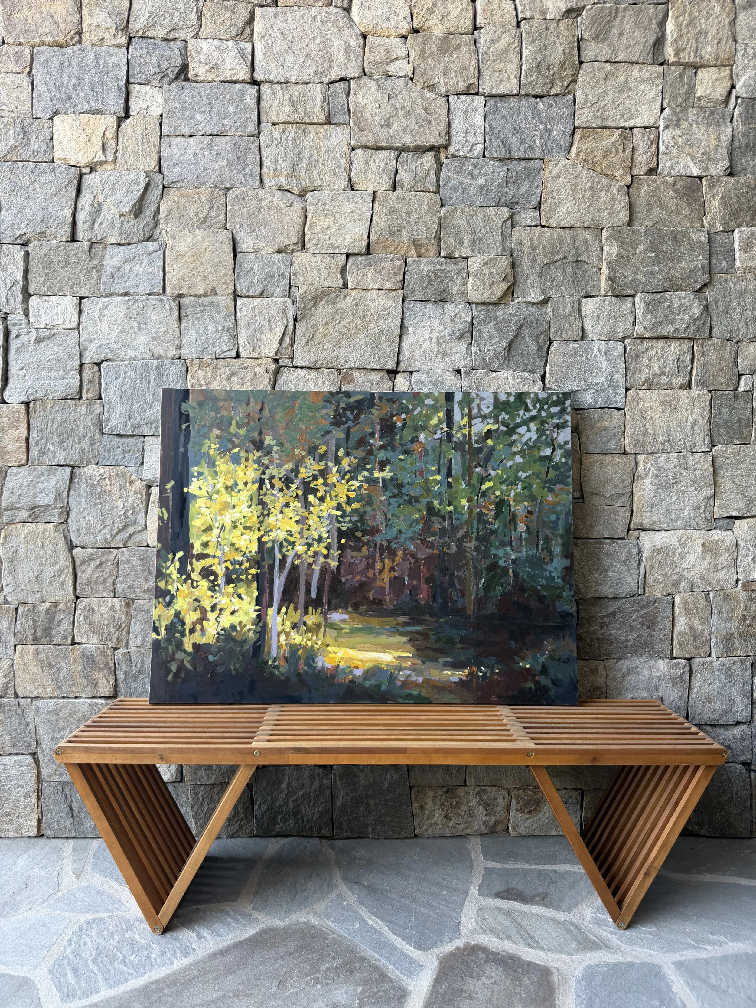 Original mixed media landscape painting by Cheyenne Trunnell displayed on a wooden bench against a stone wall, showing scale and natural light in an outdoor setting.