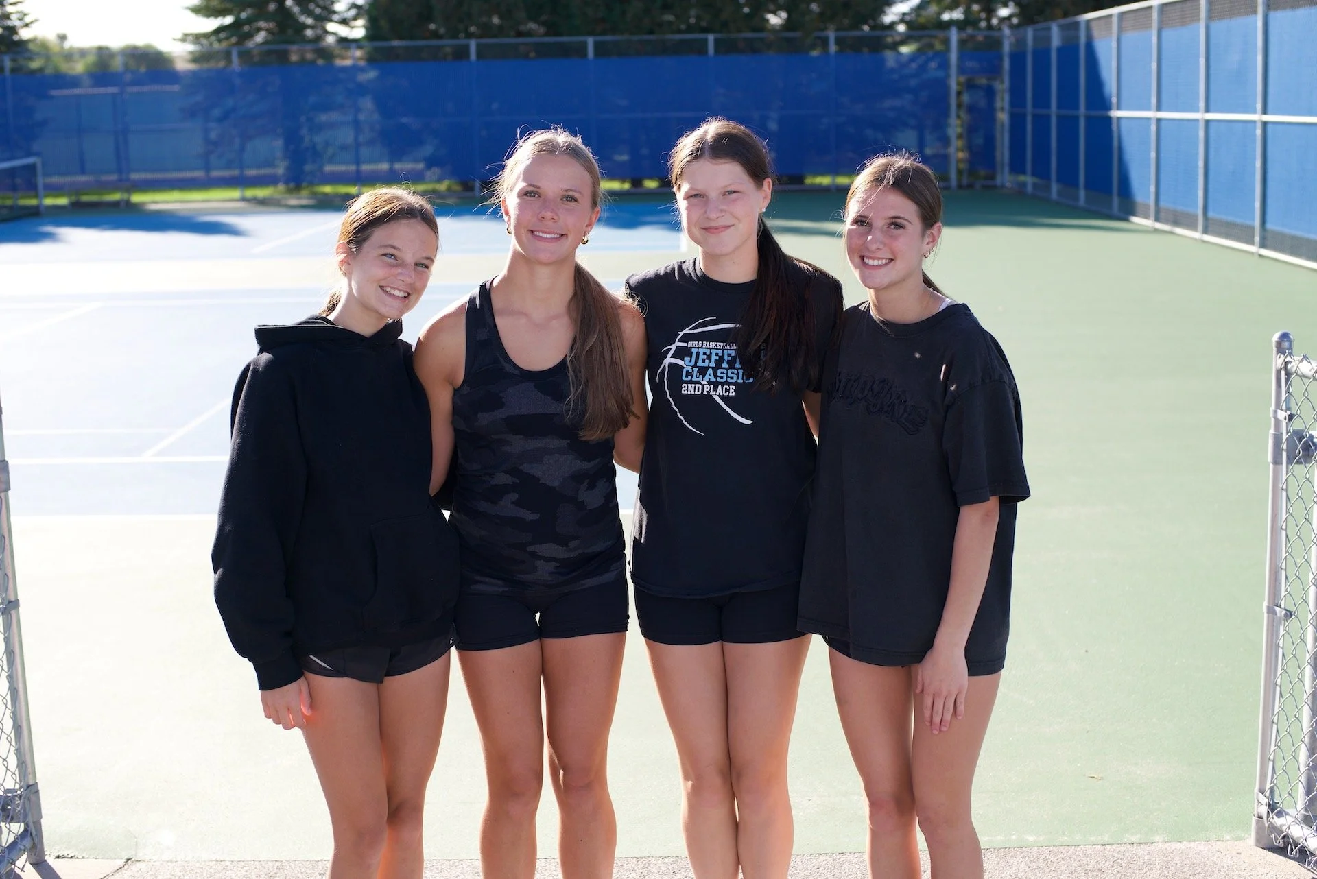 Four Hastings girls tennis players stand together beside the courts.