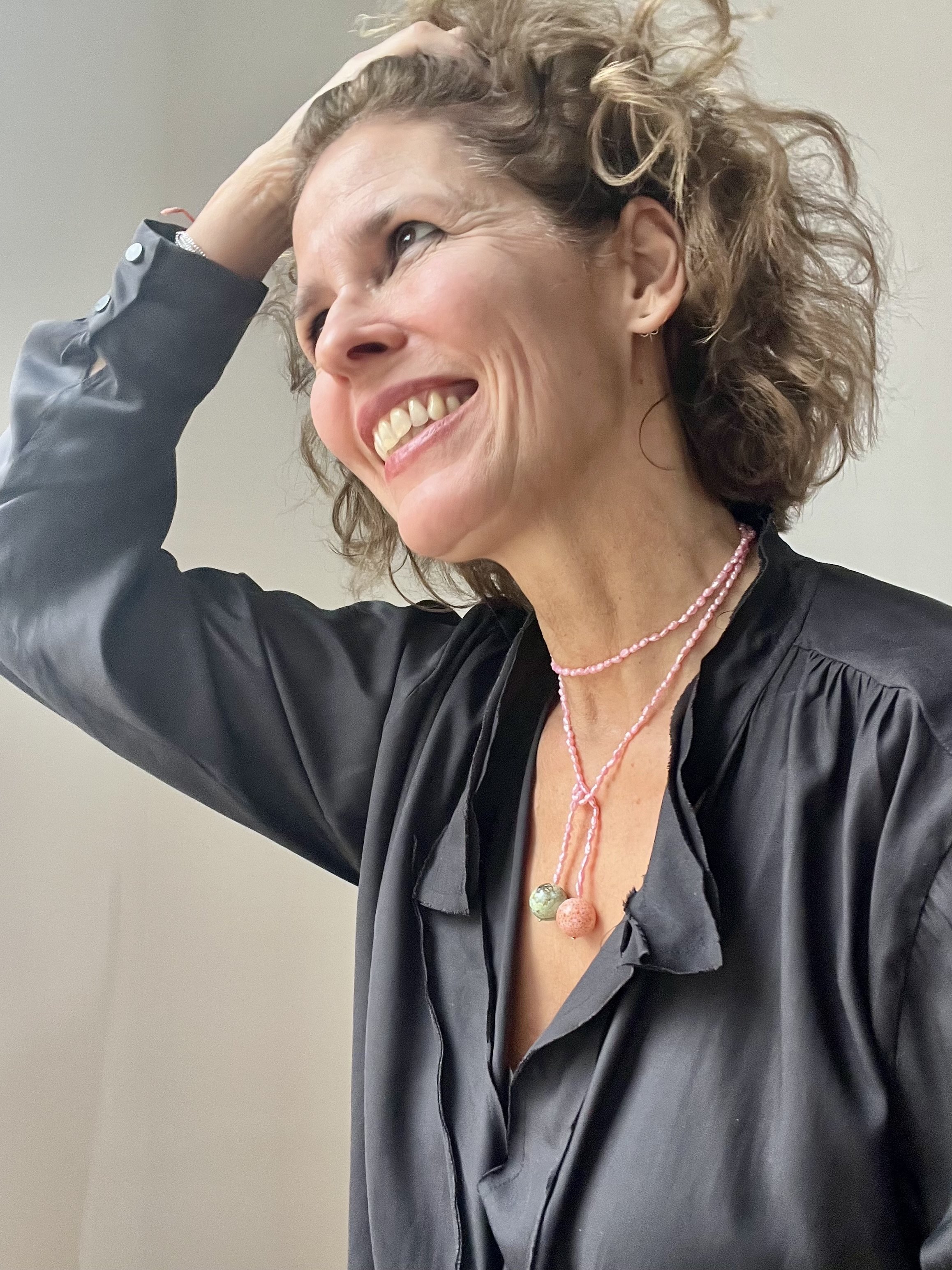 Fröhliche Frau trägt Bindi Belle Rosé-Süßwasserperlen als handgemachte Wickelkette