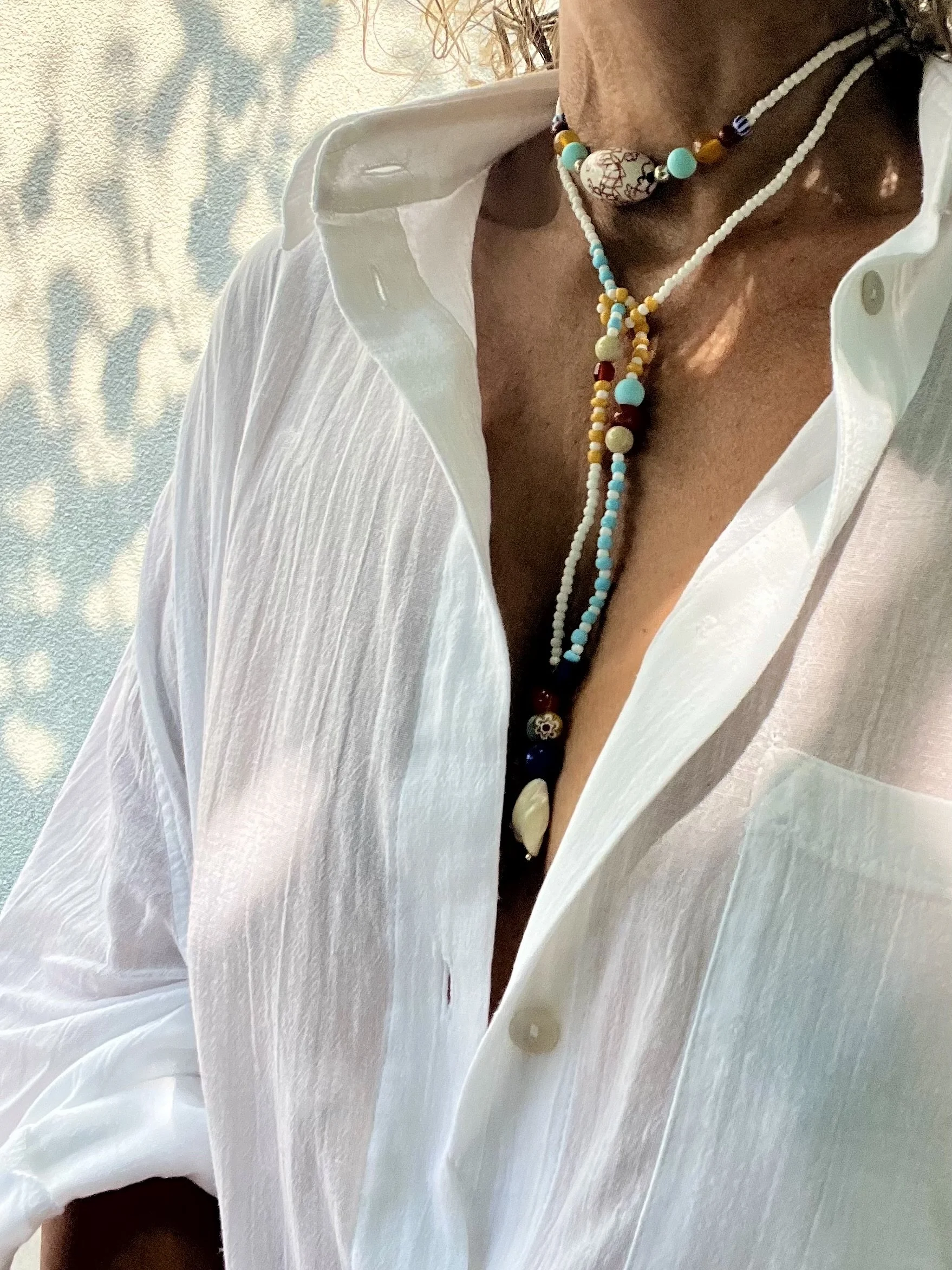 Nahaufnahme der langen Bindi Belle Halskette mit Vintage-Perlen und Anhänger auf einer weißen Bluse.