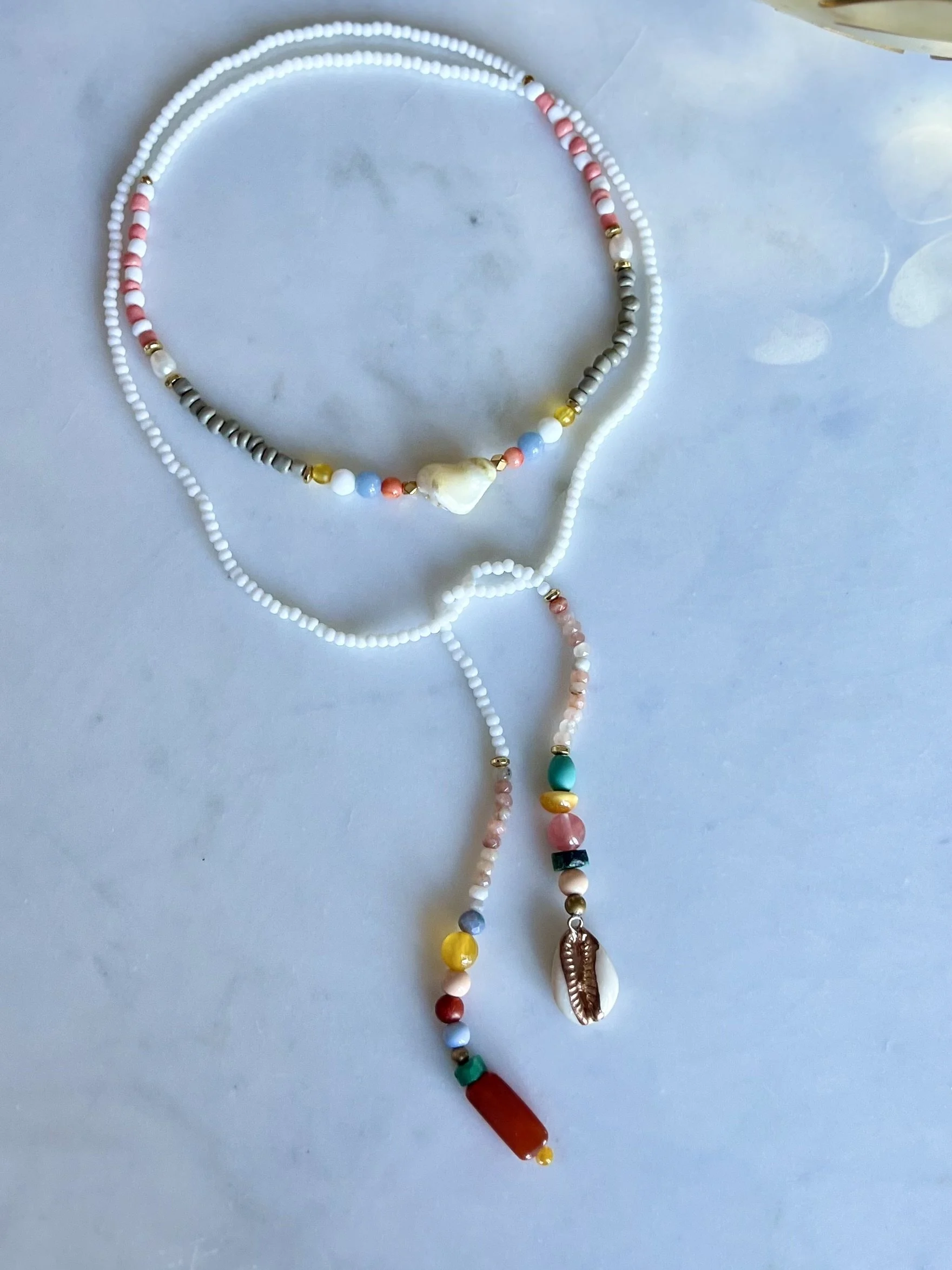 Bindi Belle Weiß-Karneol-Muschel vollständig auf hellem Untergrund mit weißen Vintage-Perlen und bunten Anhängern