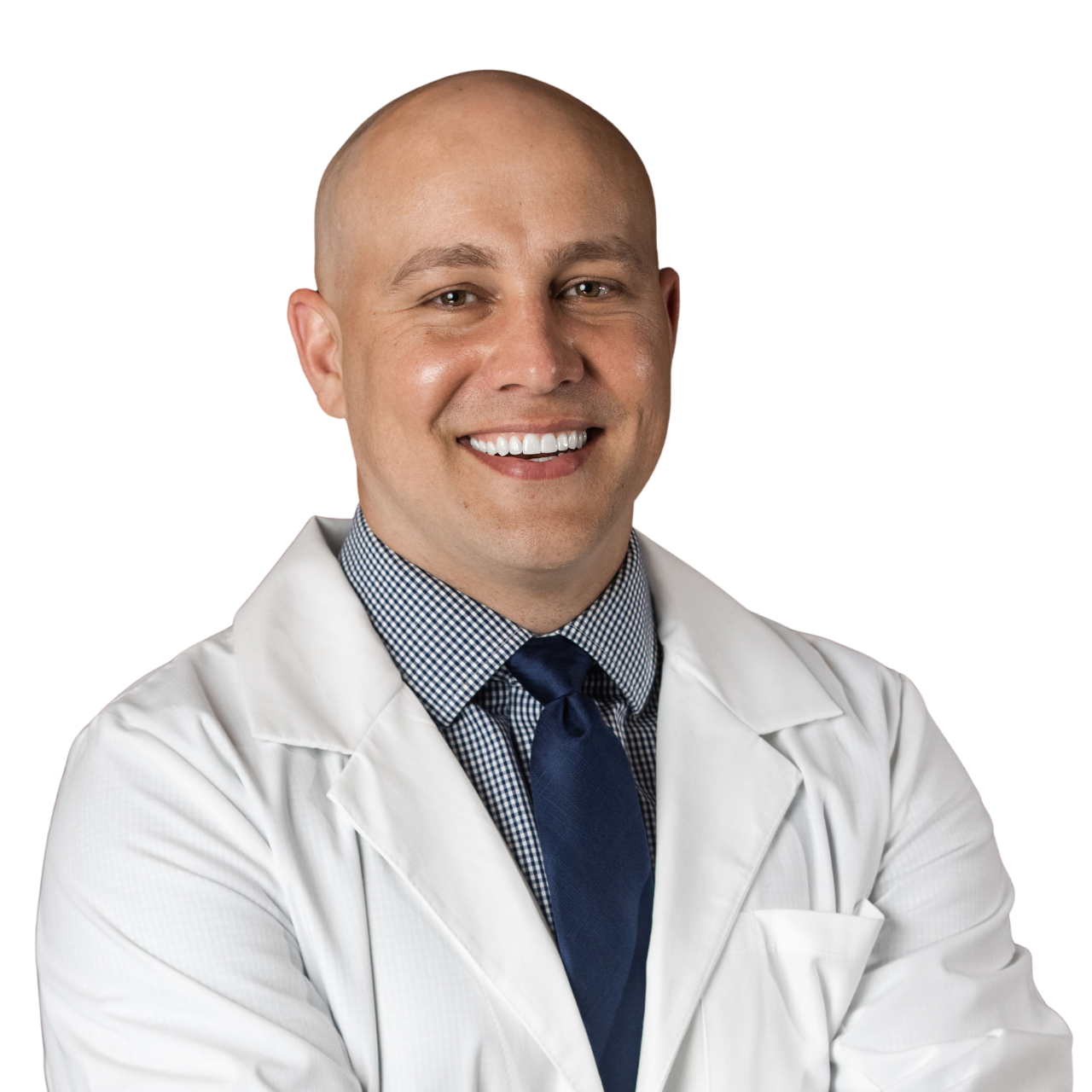 A smiling male doctor with a shaved head in a white coat and a blue tie, crossing his arms, in a professional setting.