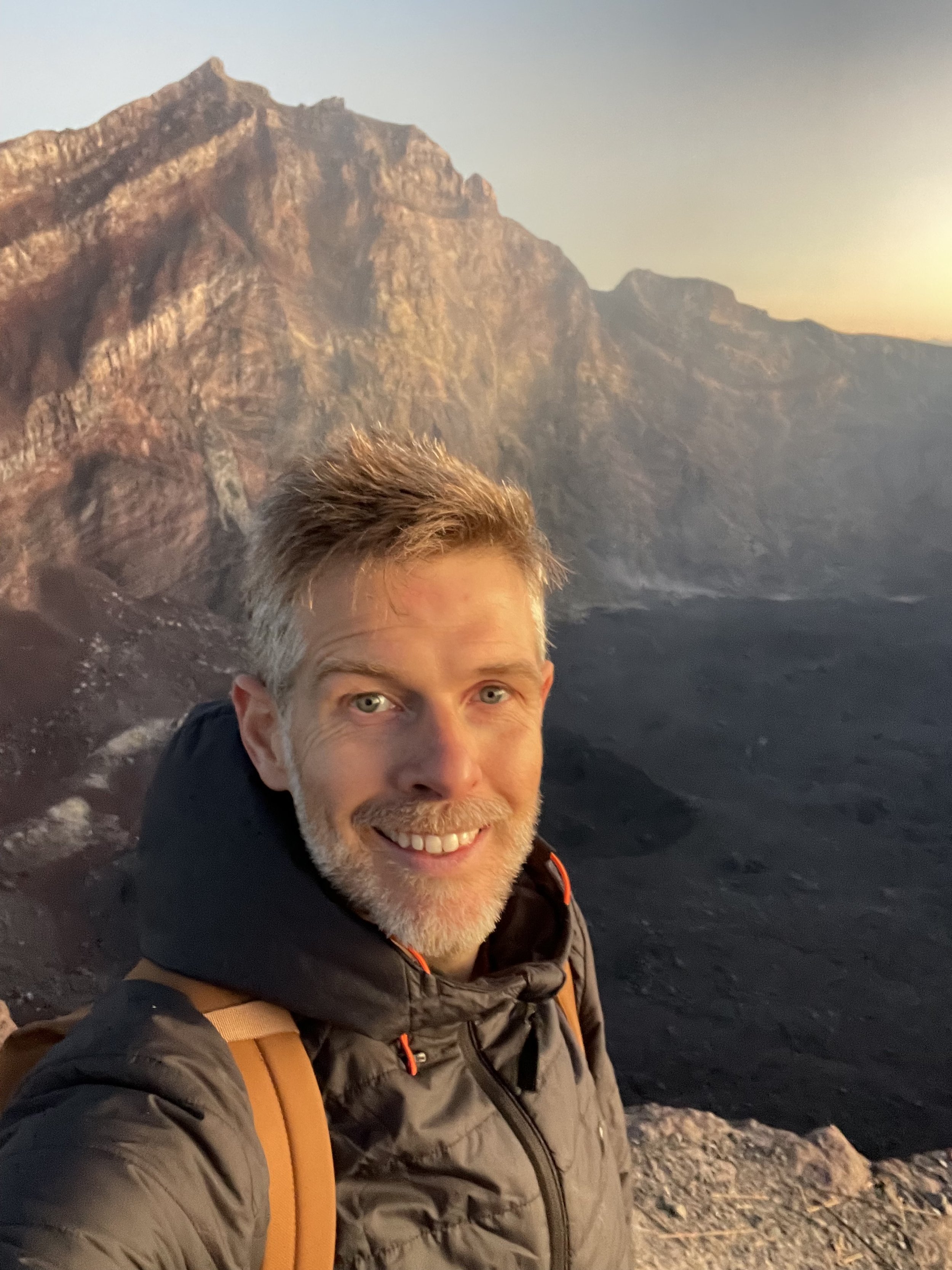 Olly Carter smiling on Mount Agung volcano in Bali with sunrise behind, embodying spark and adventure