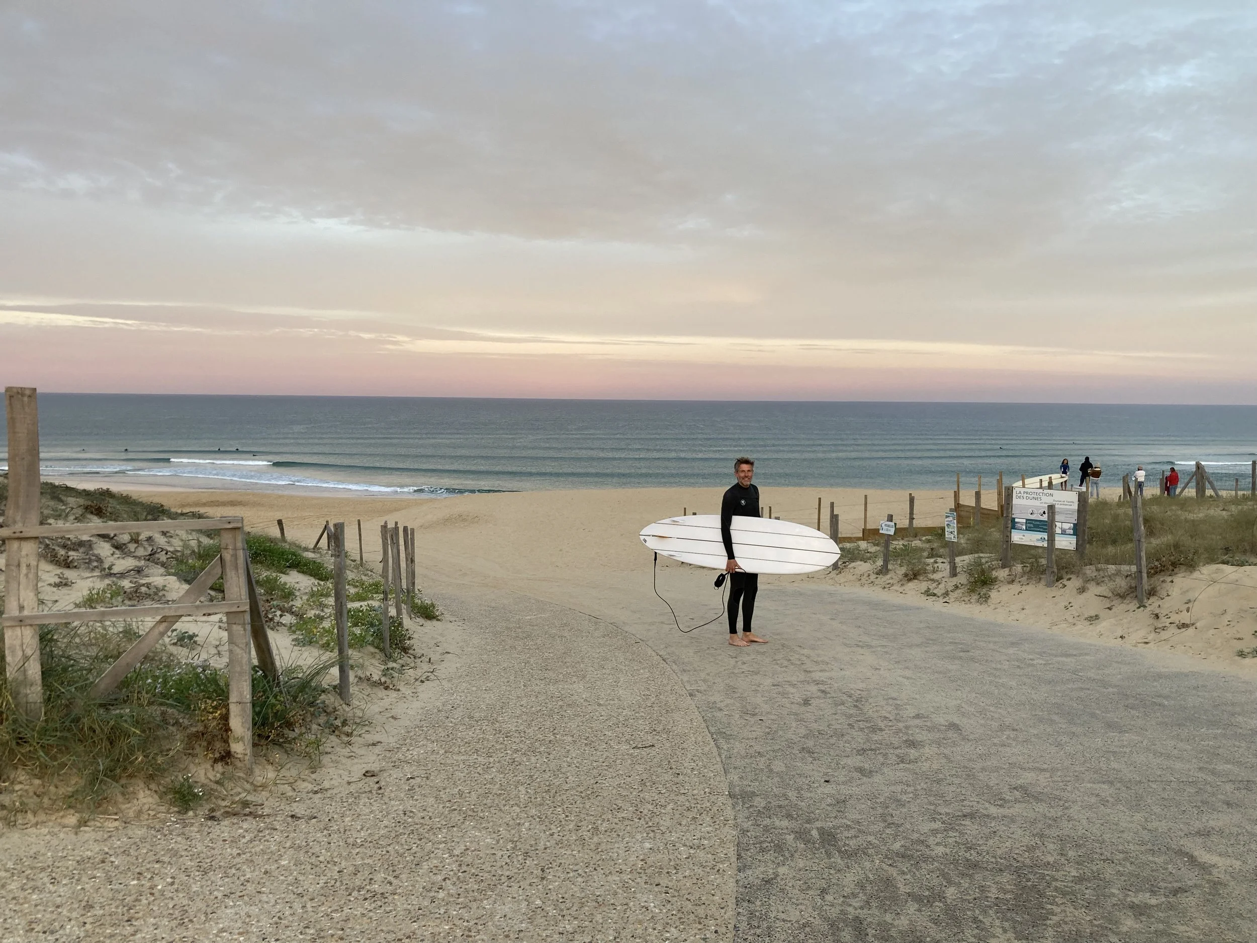 Olly Carter standing on Hossegor beach France holding surfboard, happy in his happy place