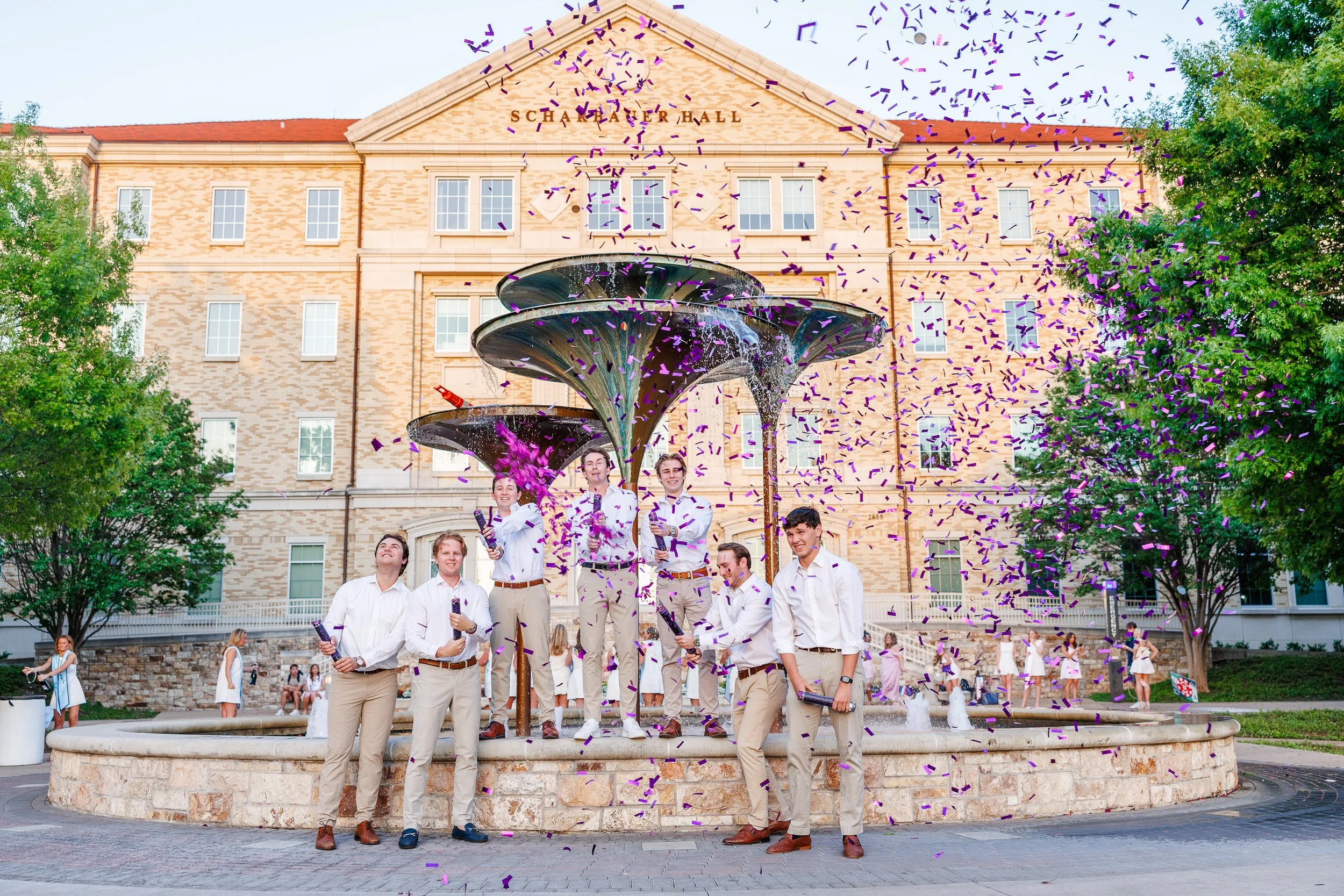 Group of TCU senior guy popping confetti in front of Frog Fountain