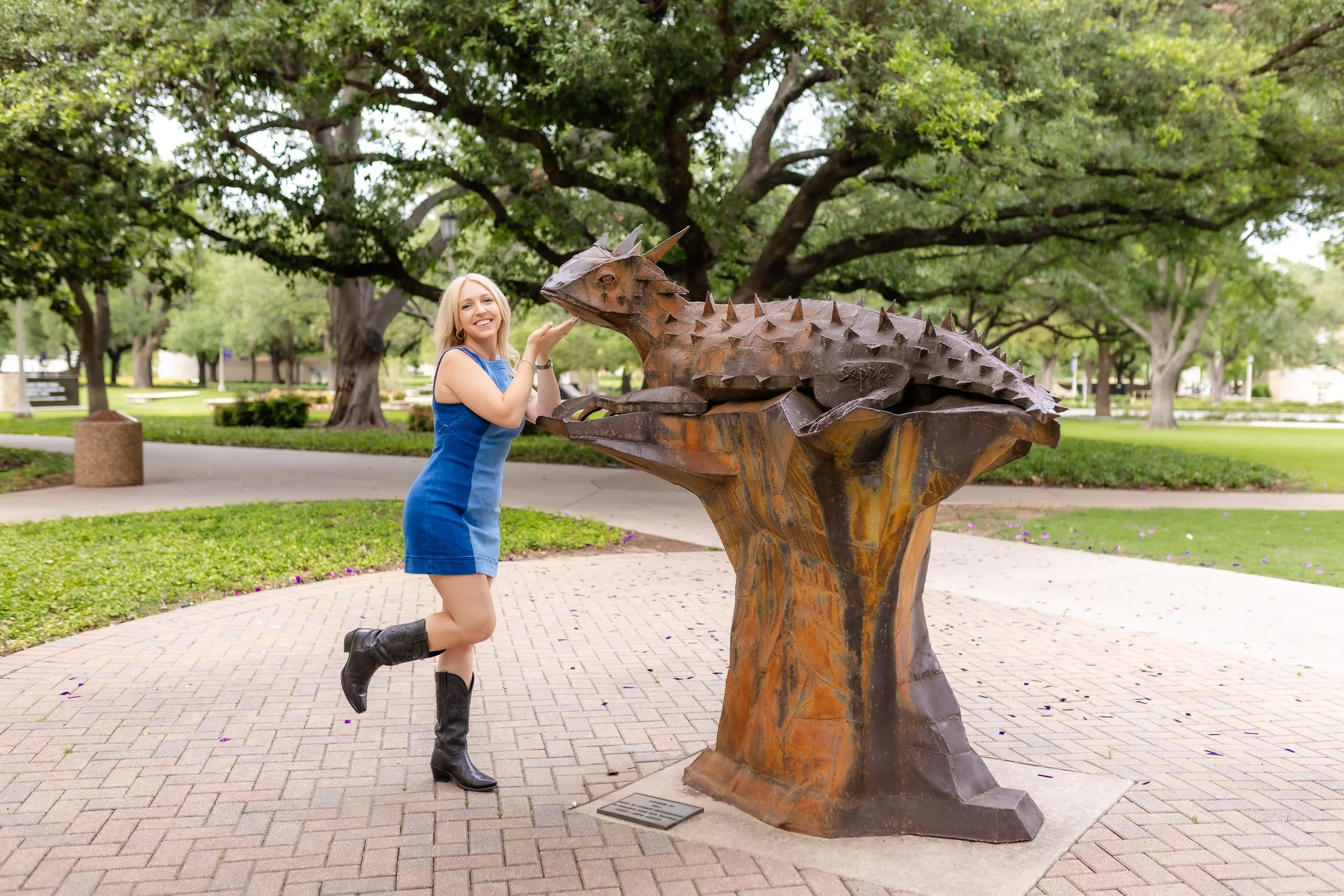 TCU senior girl in blue denim dress posing with SuperFrog statue during Fort Worth senior photography
