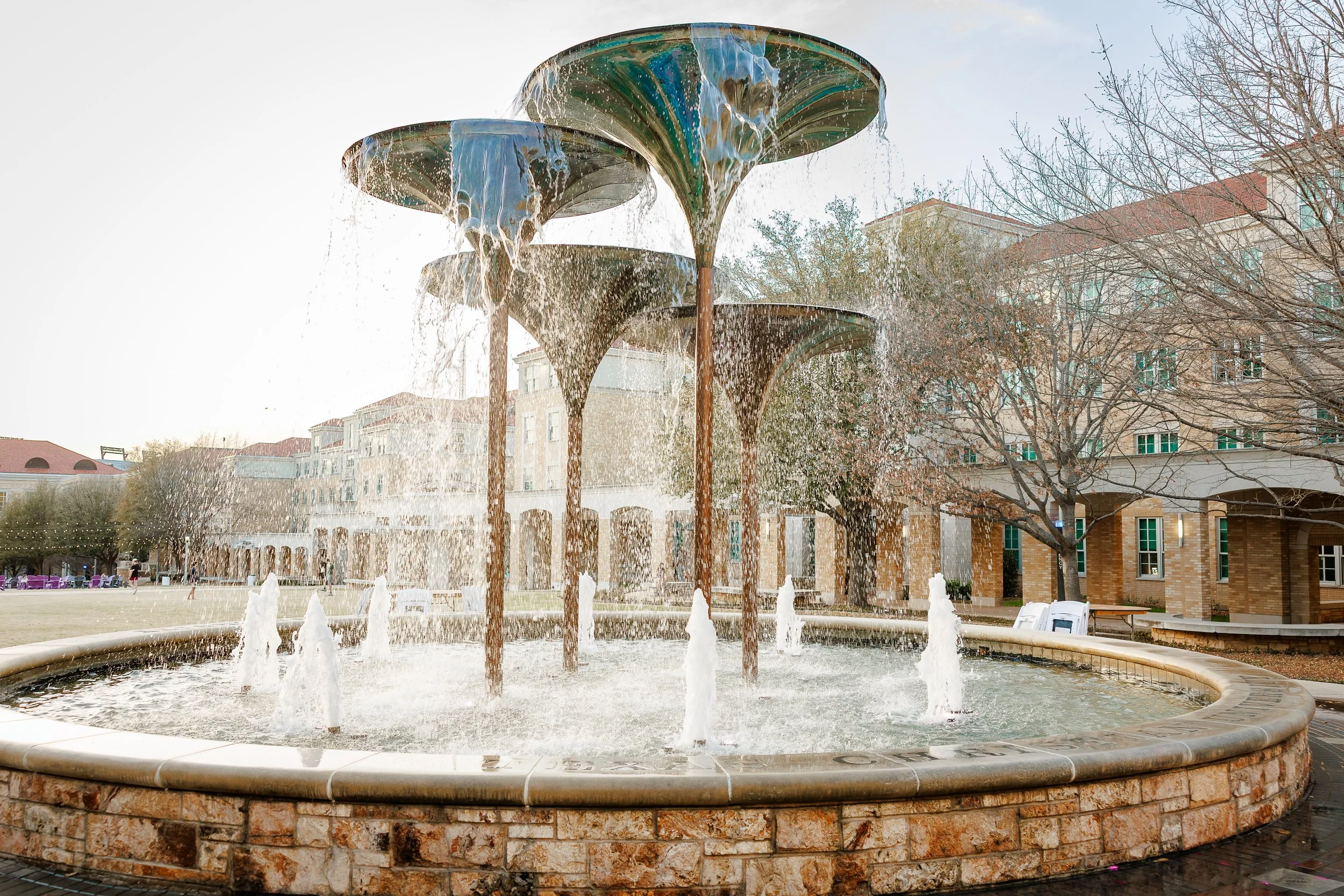 A wide view of the famous frog fountain at Texas Christian University with water cascading from the unique flower-petal-shaped sculptures. This campus landmark is a popular spot for grad photos at Texas Christian University.