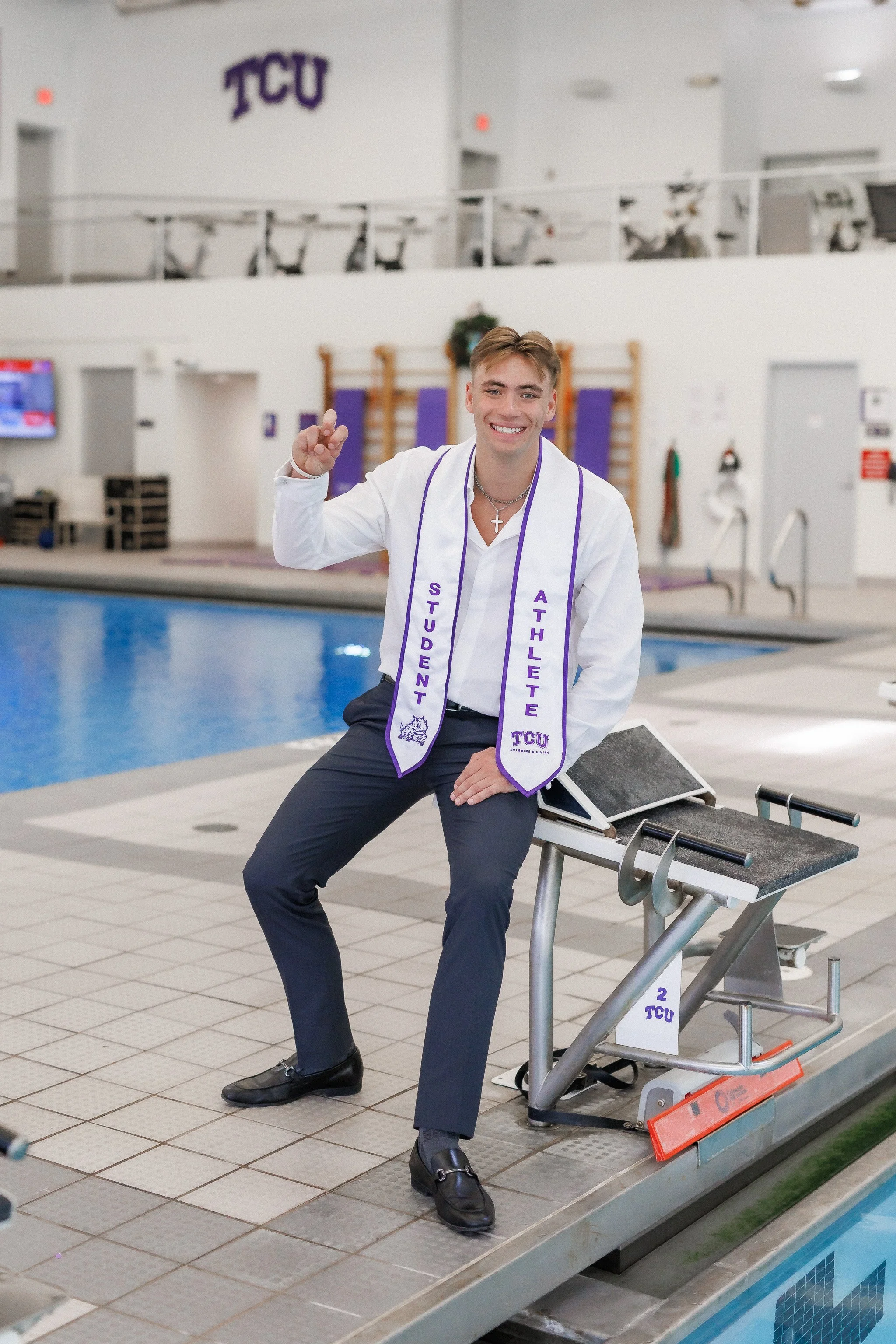 TCU Senior guy wearing white shirt and a student athlete stole sitting on starting blocks at the pool at the University Recreation Center posing for senior pictures