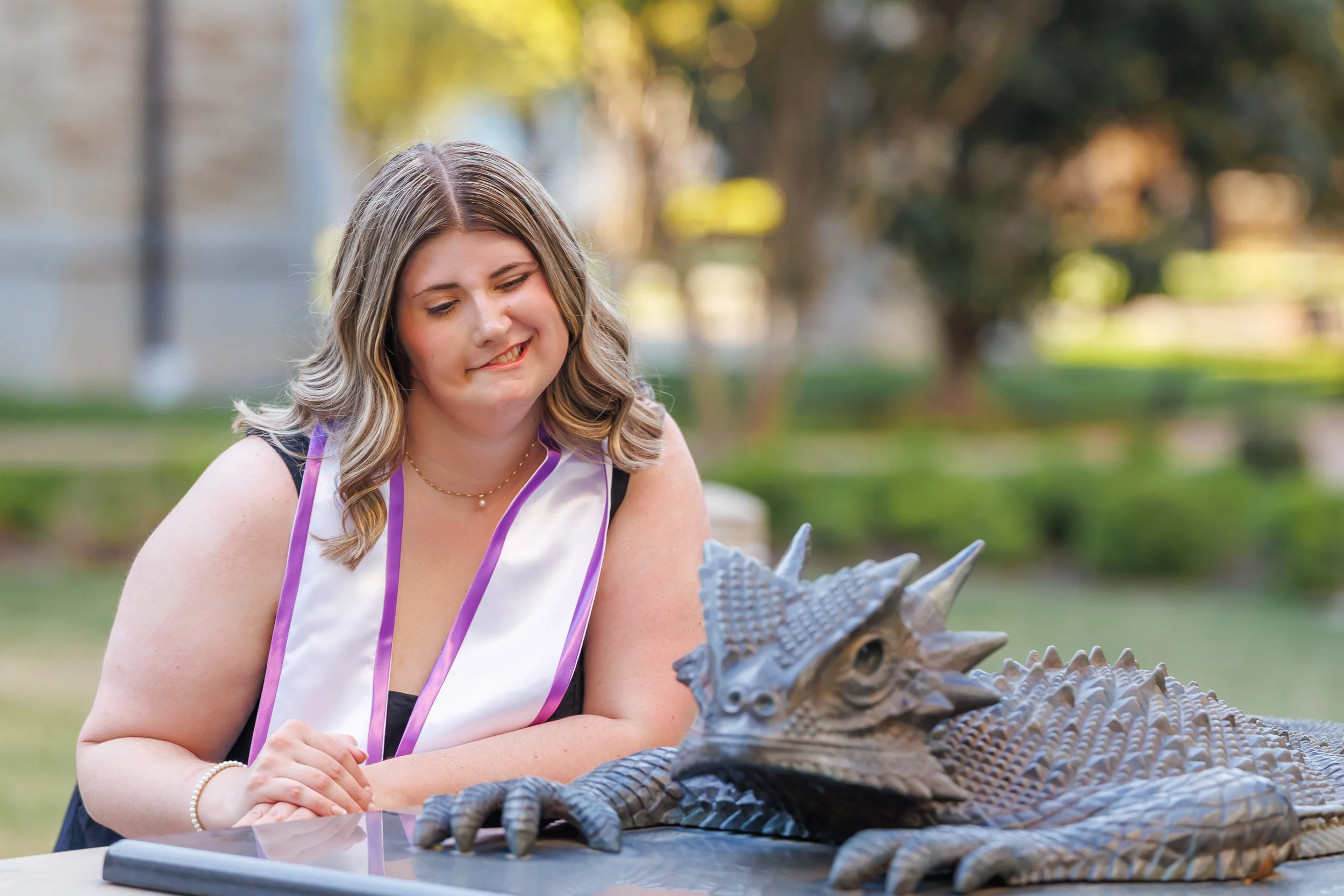 TCU senior girl in sleeveless dress posing with SuperFrog statue during Fort Worth senior photography