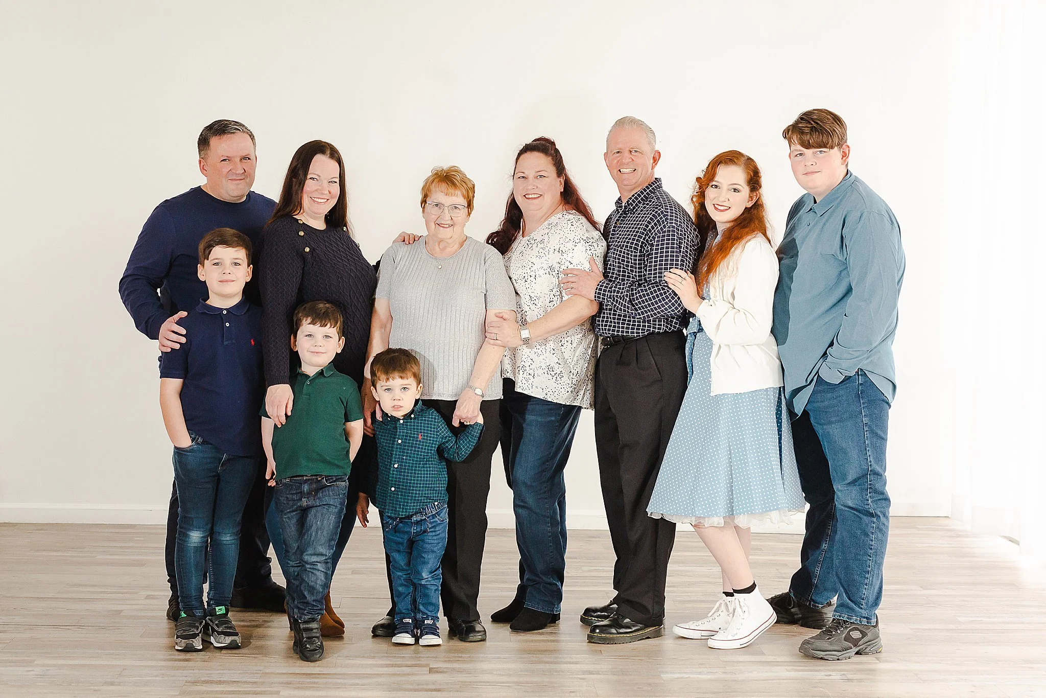extended family portrait session of a family of ten with grandmother, parents and grandparents standing and hugging in a line smiling at the camera at New Light Studio