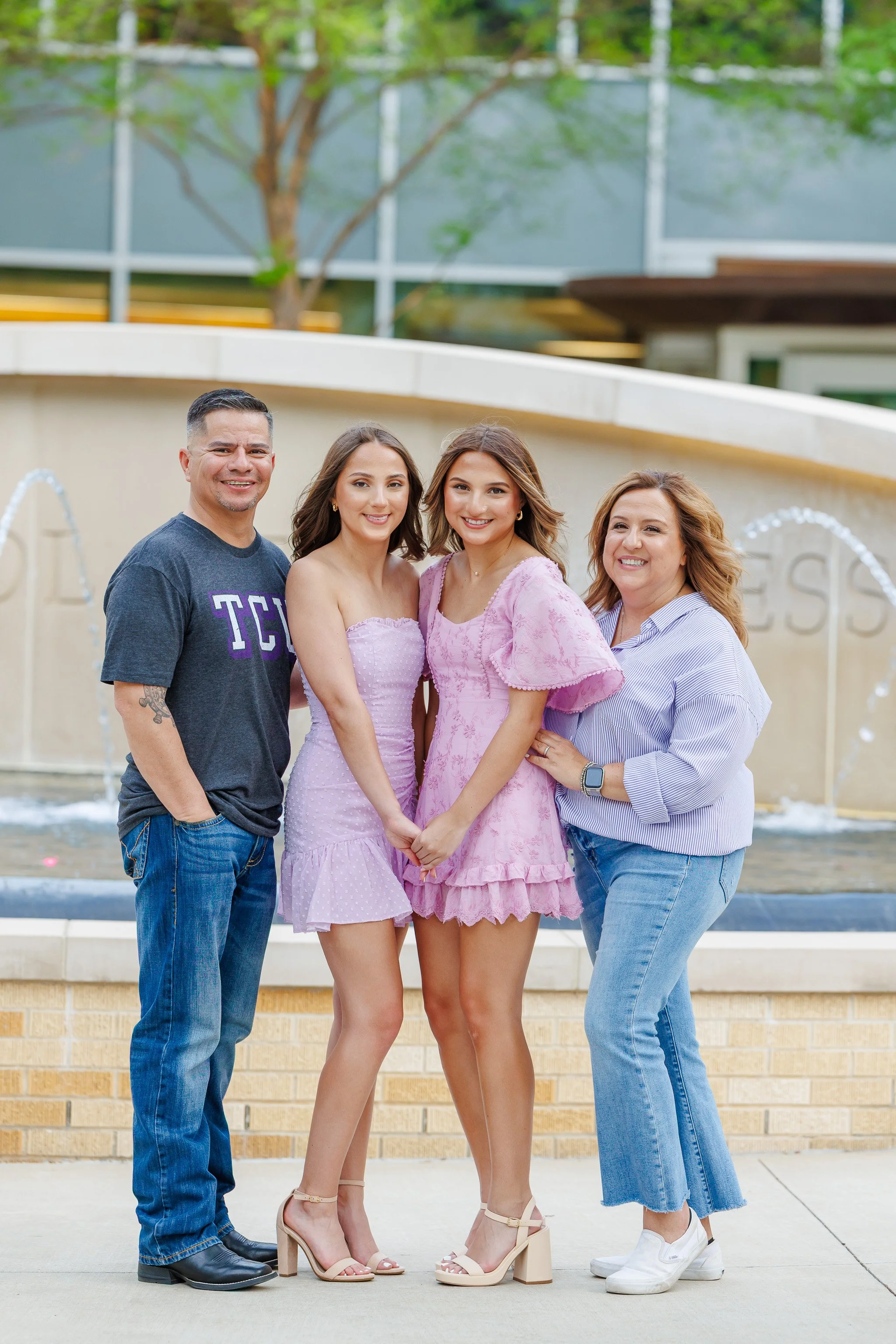 TCU Senior girls wearing lavender dresses standing with their parents in front of the water fountain at Neeley School of Business posing for senior pictures