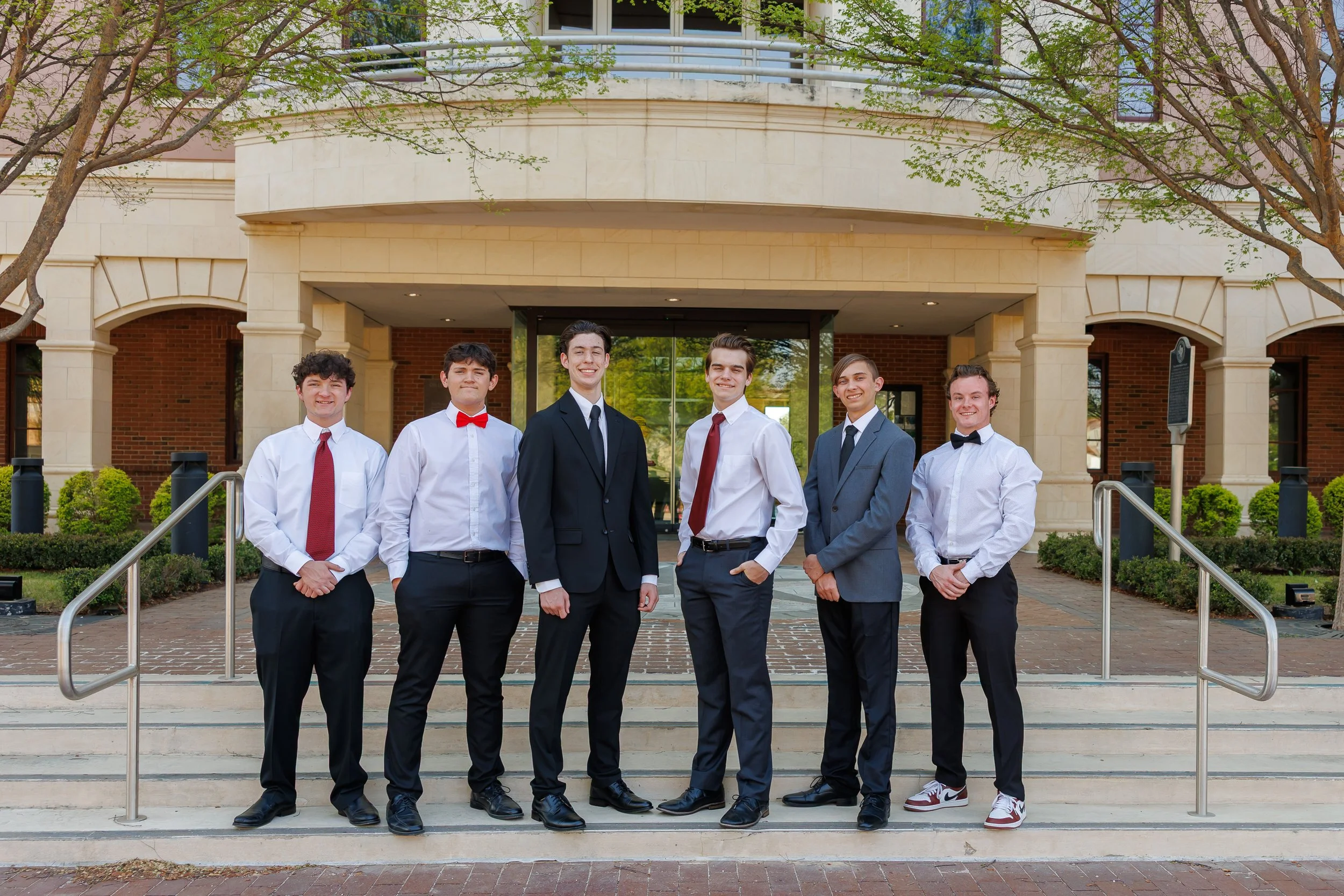 Six highschool senior guys posing for senior pictures on the steps of Colleyville Library smiling at the camera wearing dress clothes