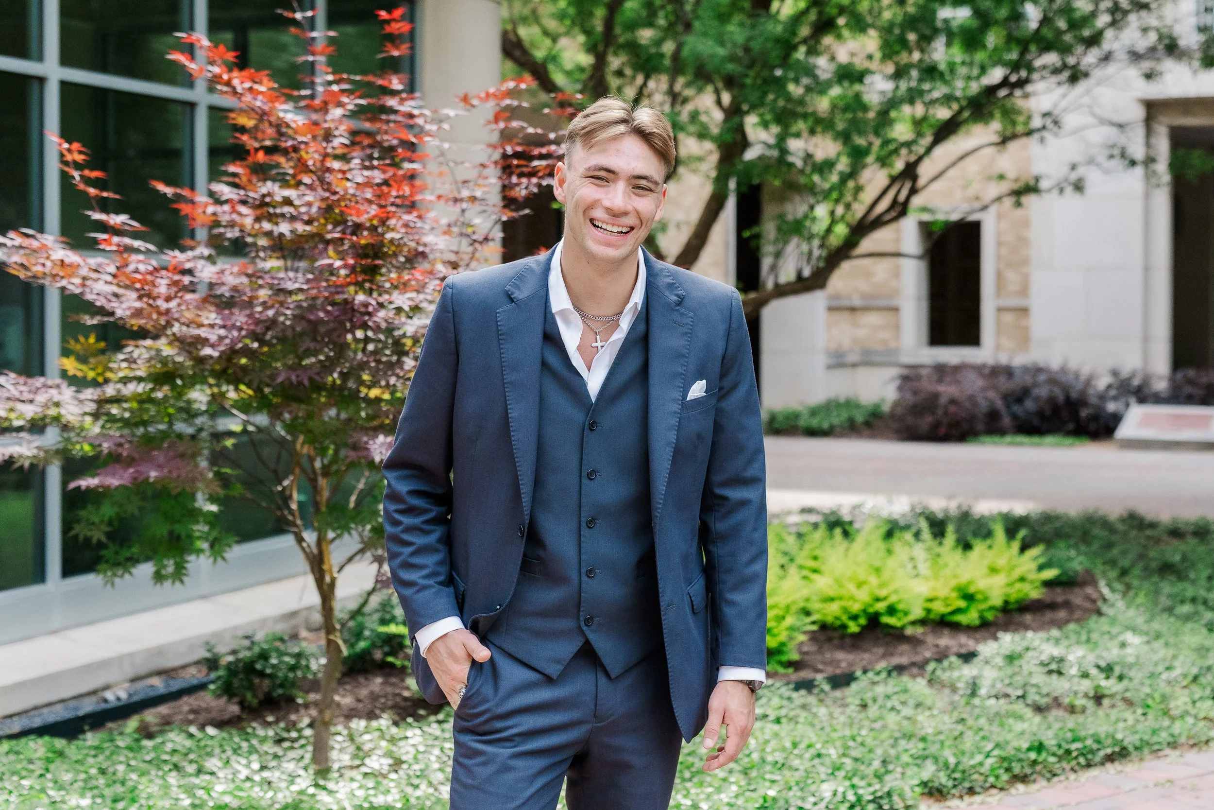 TCU senior guy wearing a grey suit standing in The Commons for senior pictures