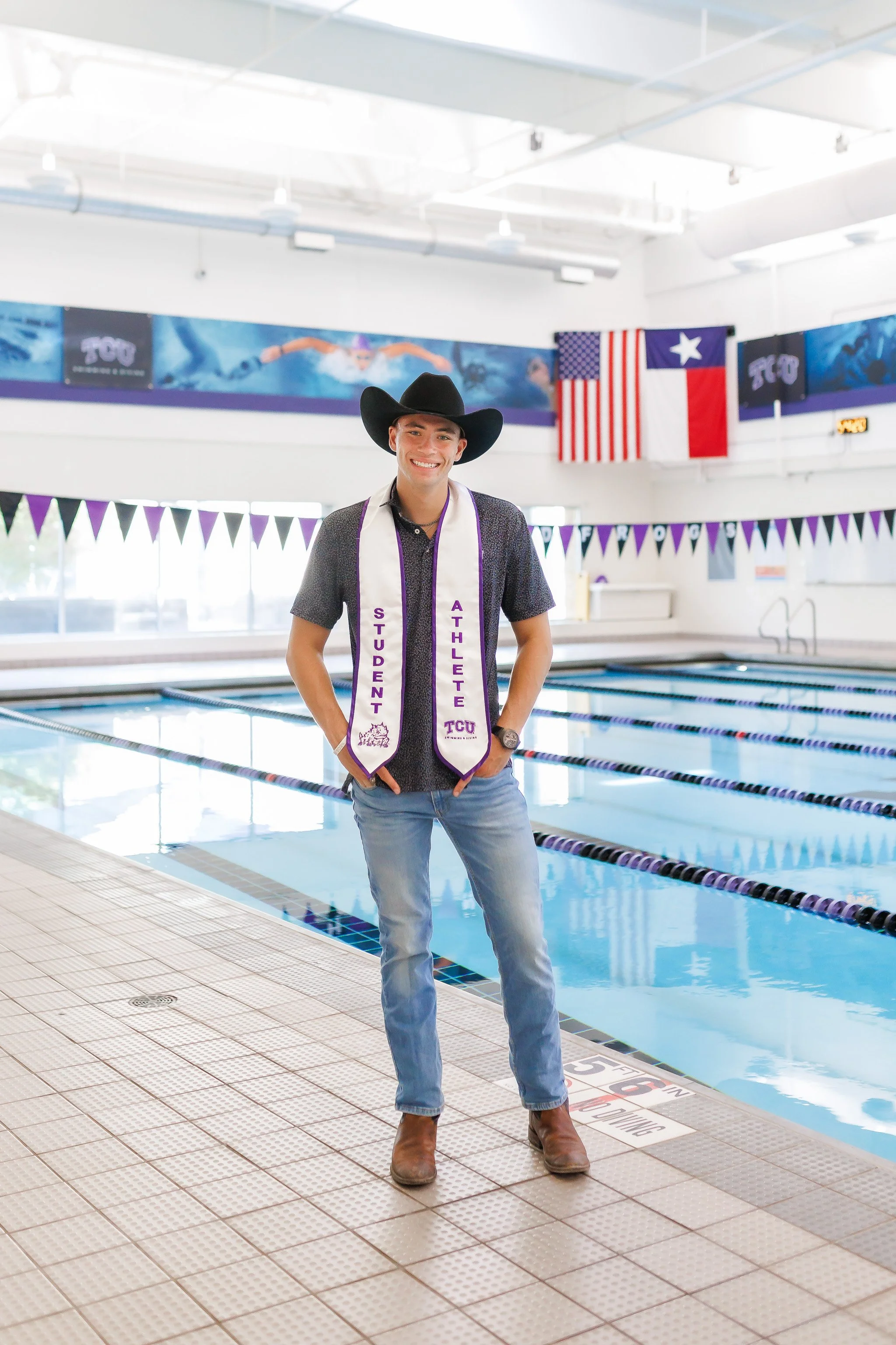 TCU Senior guy wearing a black cowboy hat and student athlete stole, while standing at the side of the pool at the University Recreation Center posing for senior pictures