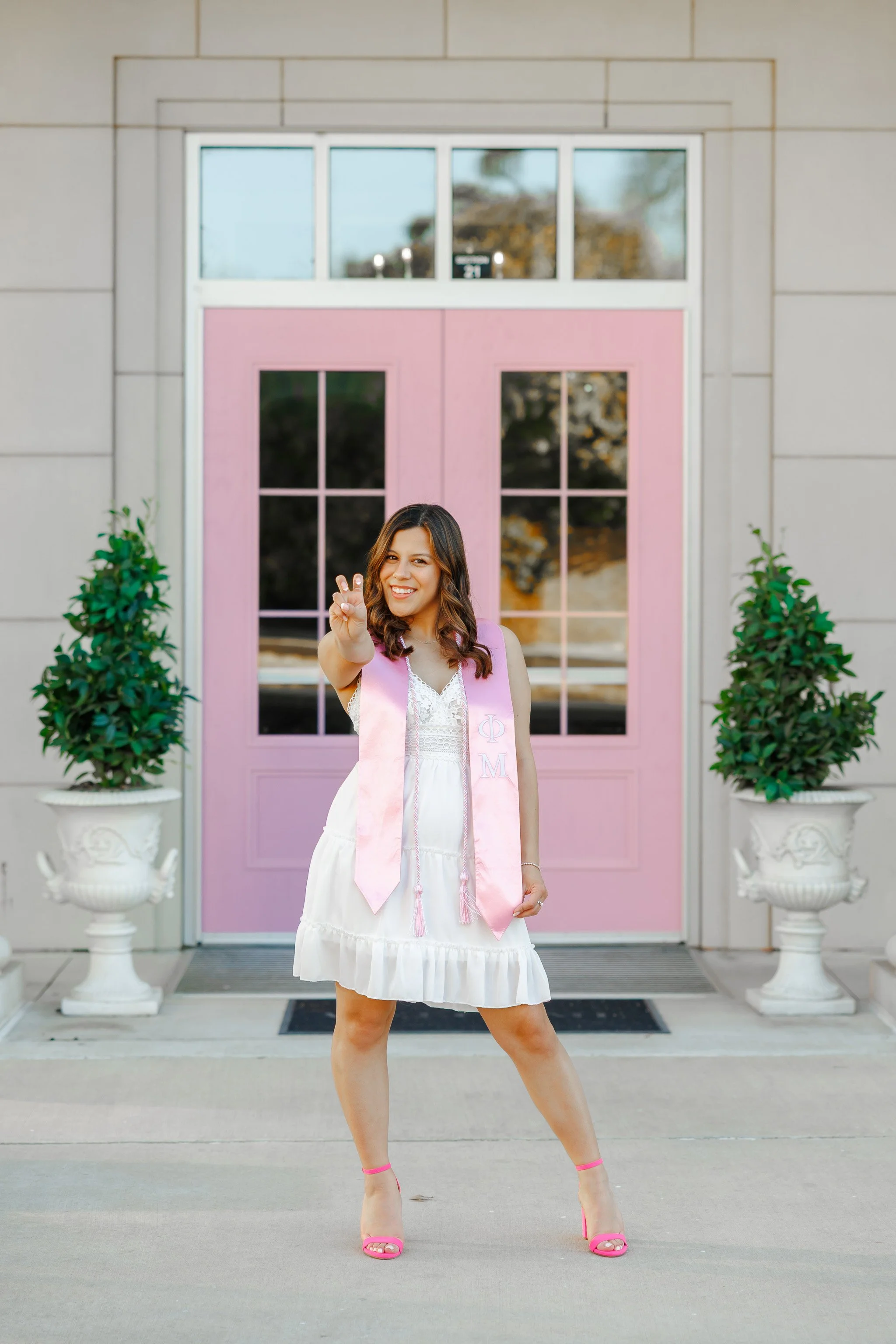 TCU senior girl in white dress with pink sorority stole posing by Phi Mu sorority house for Fort Worth graduation photos