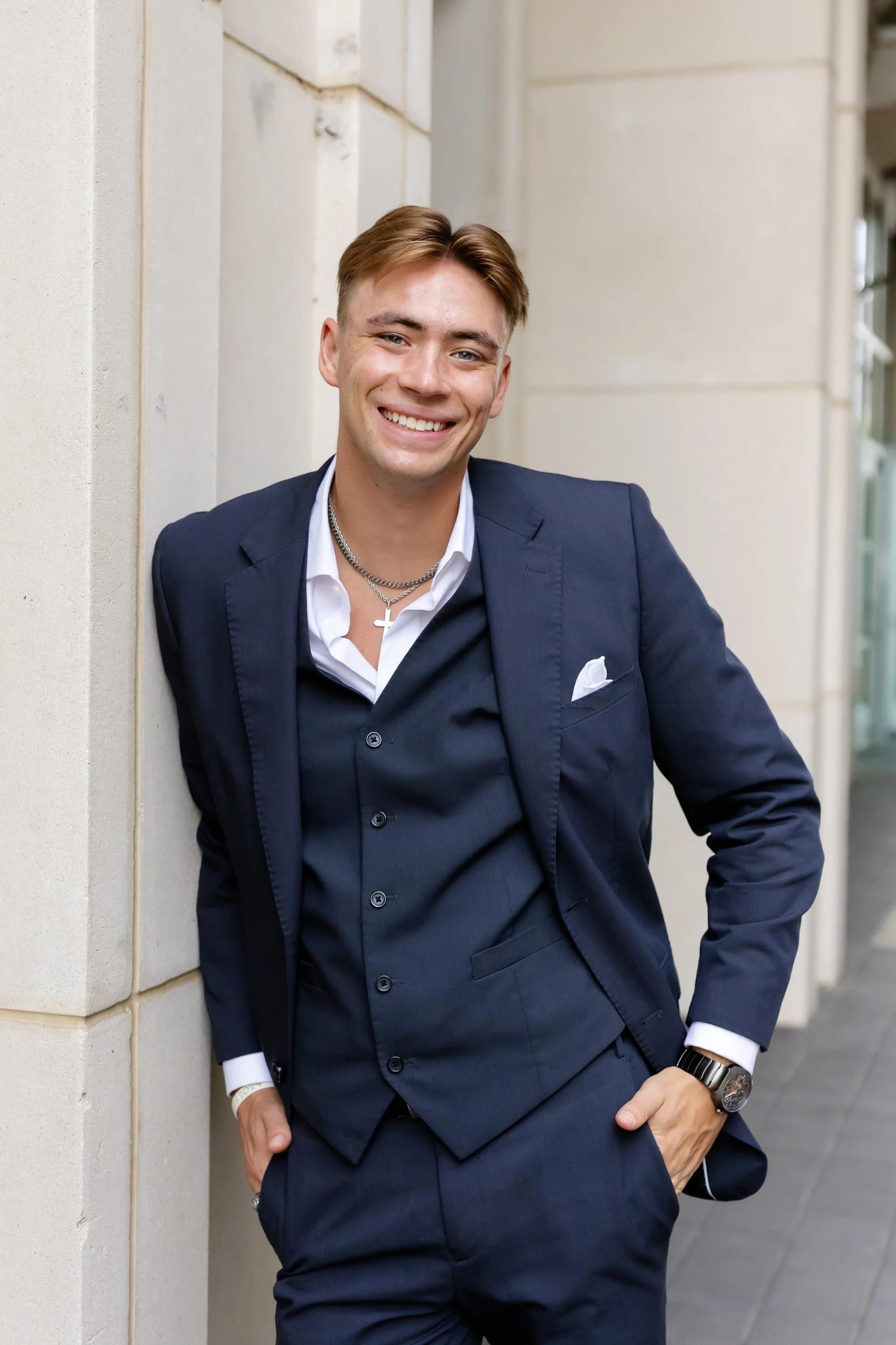 TCU senior guy wearing a grey suit leaning against the archway of The Commons for senior pictures