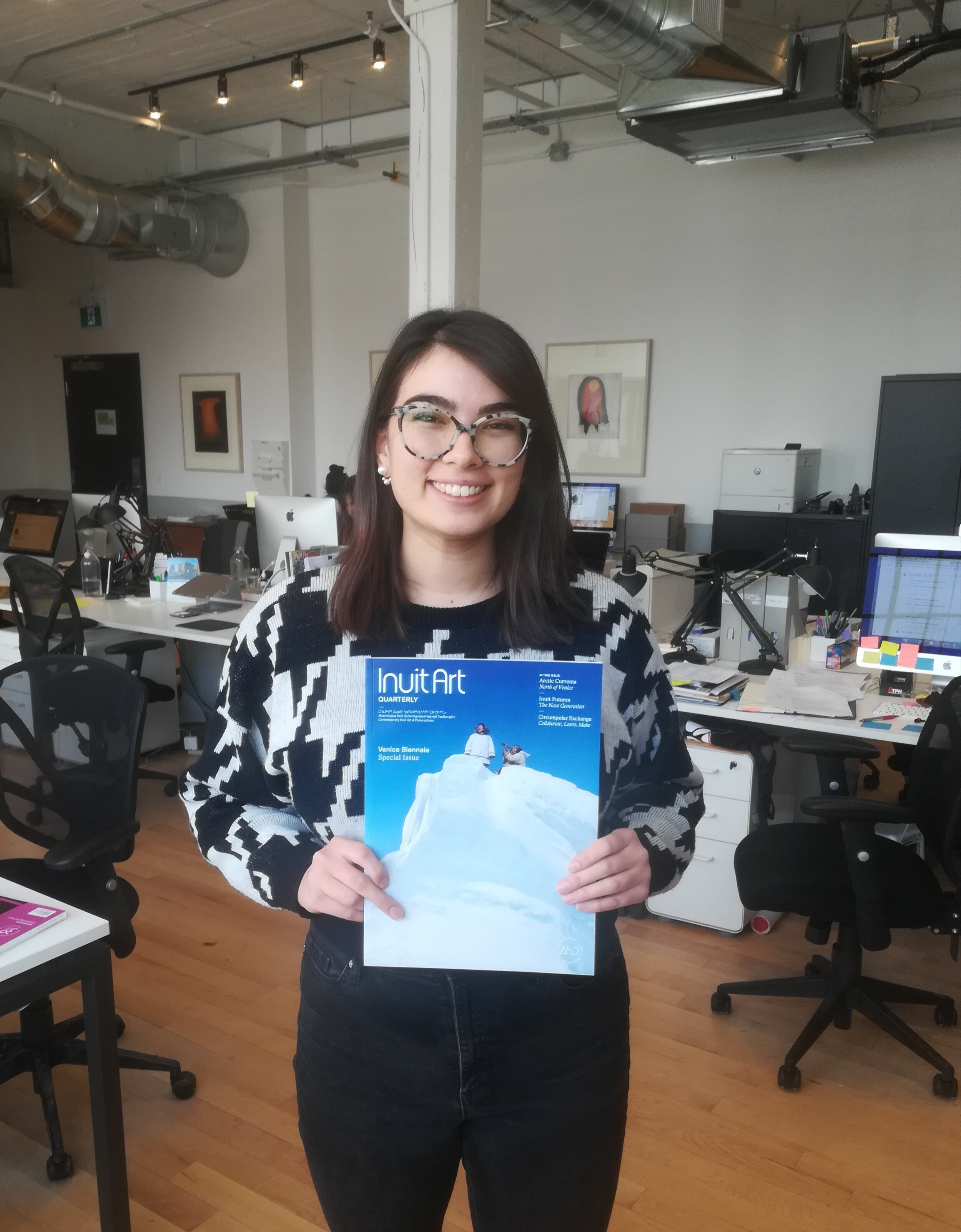  Emily at the  Inuit Art Quarterly  office holding a copy of the  Venice Biennale Special Issue  (2019), for which she worked as a Contributing Editor. Photo courtesy of Emily Henderson. 