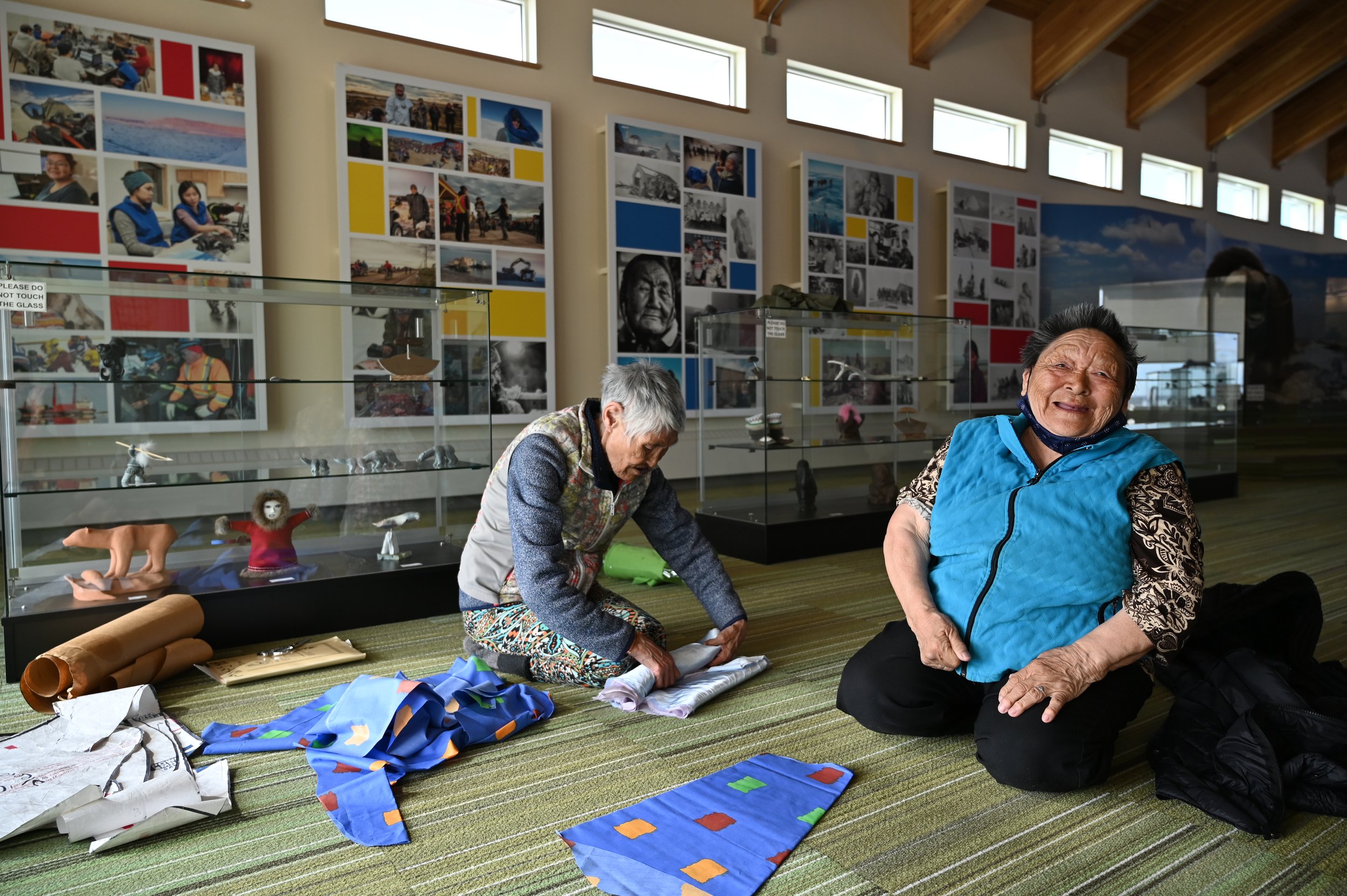  Inside the Kivalliq Regional Visitor Centre in Rankin Inlet. Helen Iguptak (left) workshop instructor and Elder, explains the components of the  tuili  (the garment used by women as parkas and to carry babies on our backs) to our oldest student, Mon
