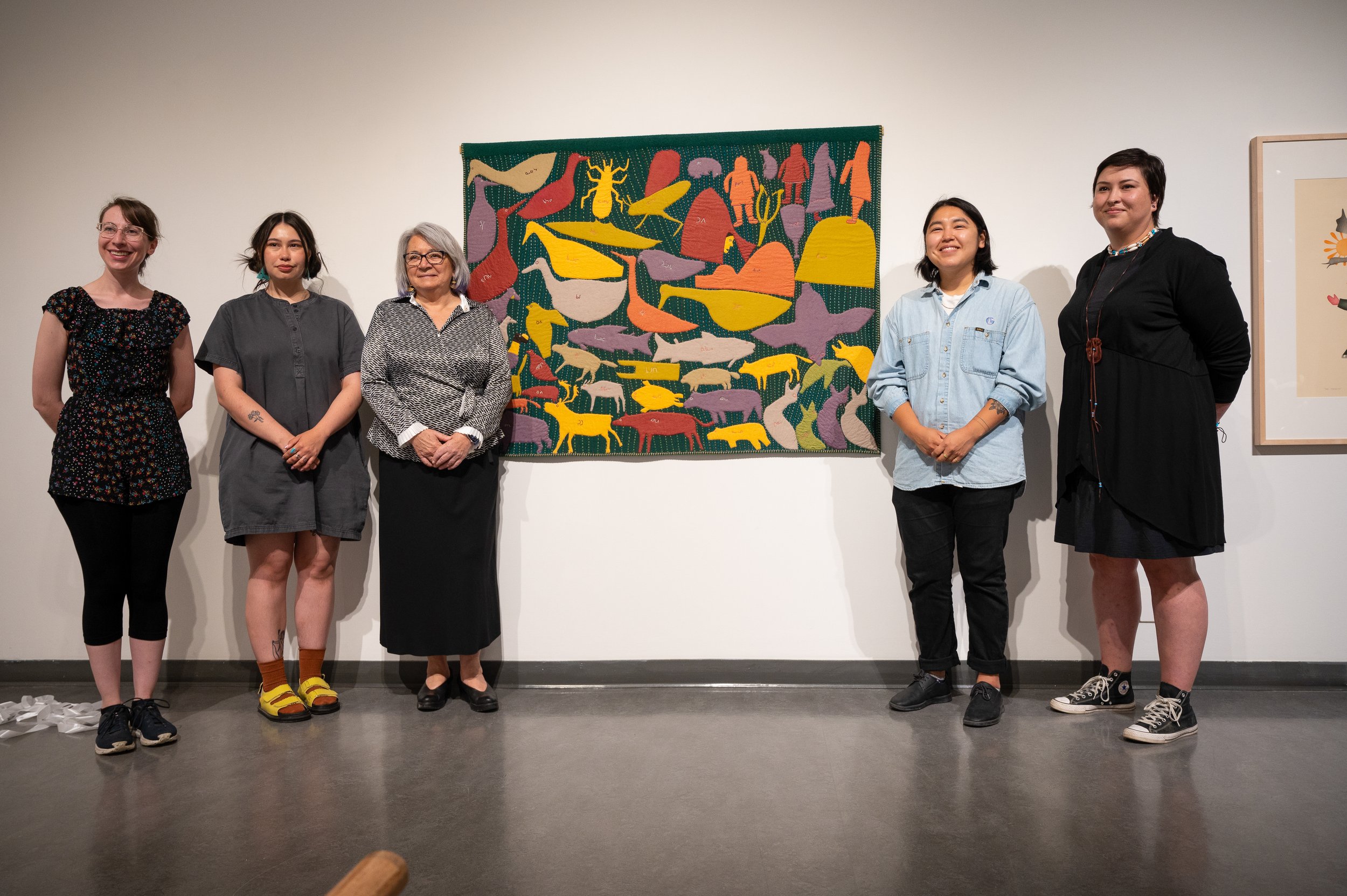   TETHER  co-curators Teresa Vander Meer-Chassé, Leanne Inuarak-Dall, Darcie “Ouiyaghasiak” Bernhardt, and Heather Von Steinhagen, with the Governor General, Her Excellency the Right Honourable Mary Simon, pose in front of a wall hanging by Marion Tu
