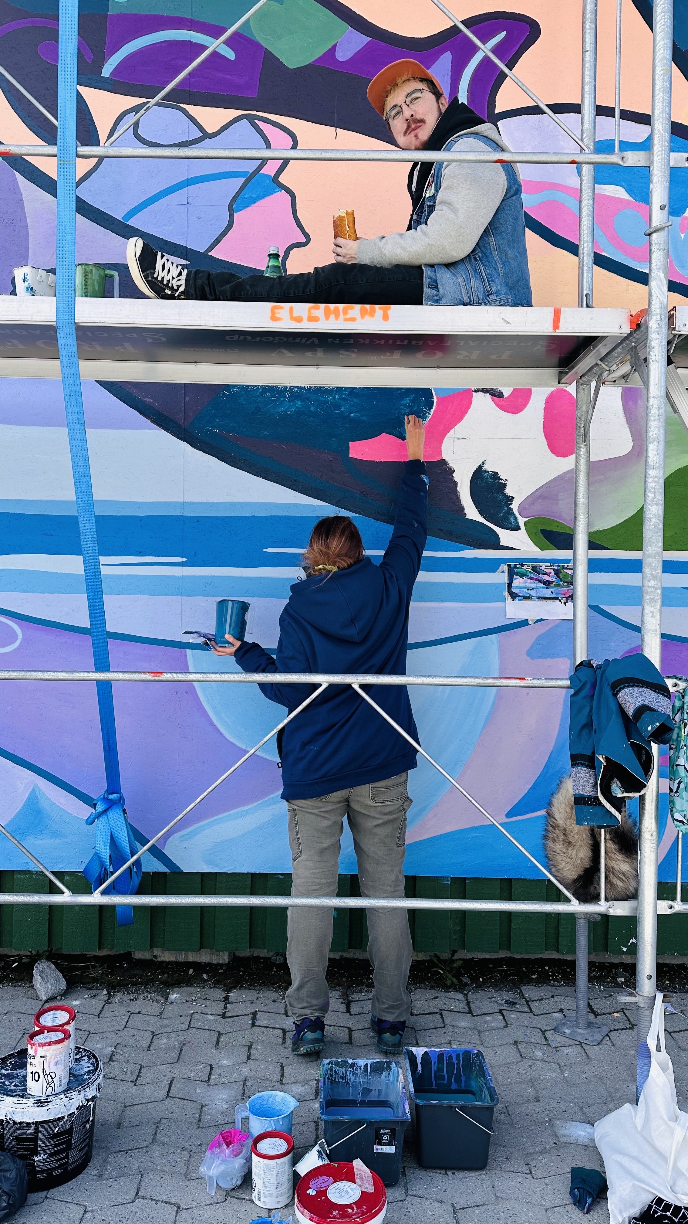  Ilinniaqtuit Bronson Jacque and Yvonne Moorhouse paint part-of the mural at the Nunatta Atuagaateqarfia during the Nuuk Nordic Festival. Nuuk, Greenland. May 2023. Photograph by Sacha. 