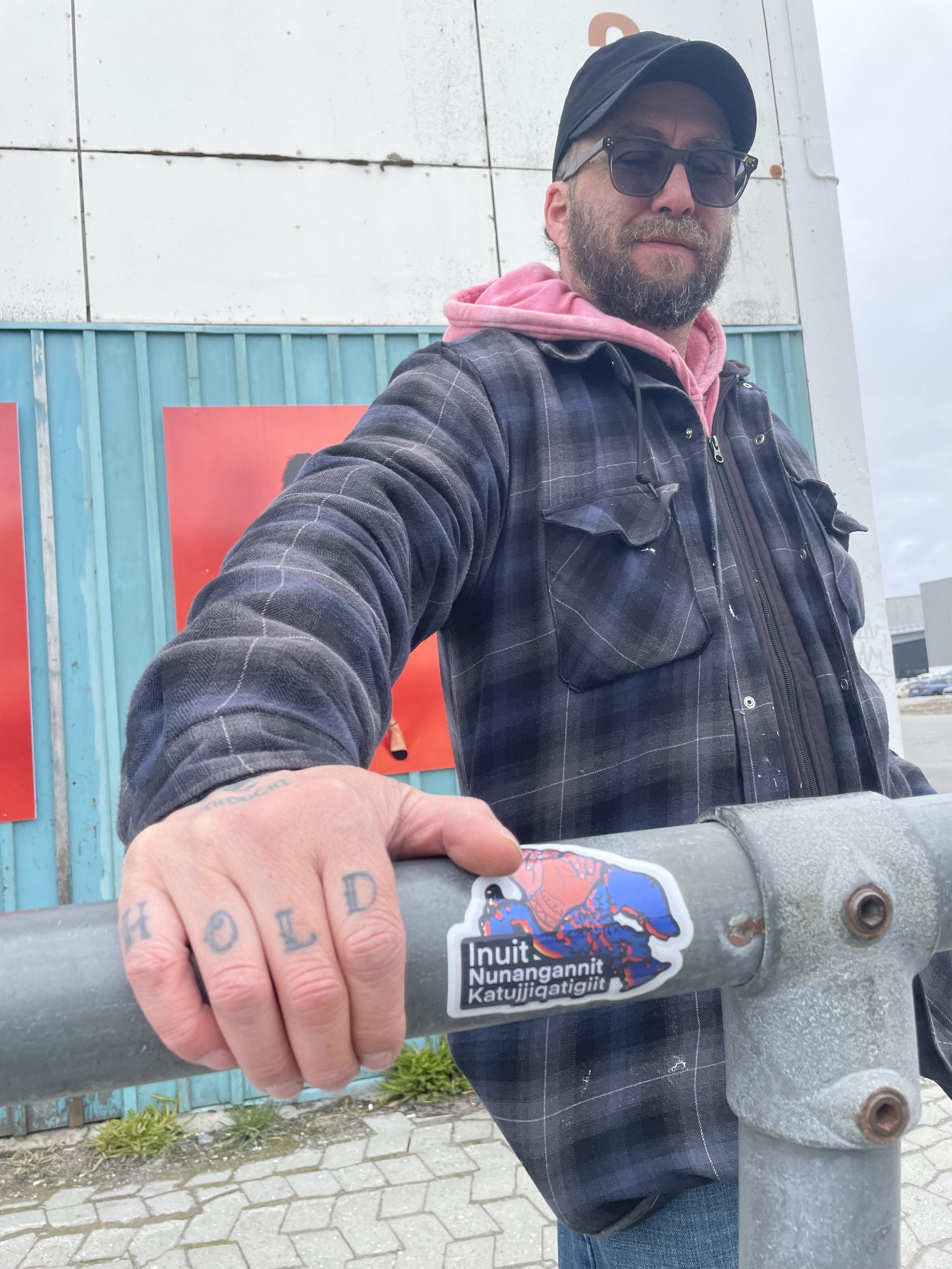  Photograph of Ilinniaqtuit alumni, Jason Sikoak, with their hand beside the Bronson Jacque and Jessica Winter’s sticker designed for  Inuit Futures  at the Nuuk Nordic Festival. Nuuk, Greenland. May 2023. Photograph by Danielle Miles. 