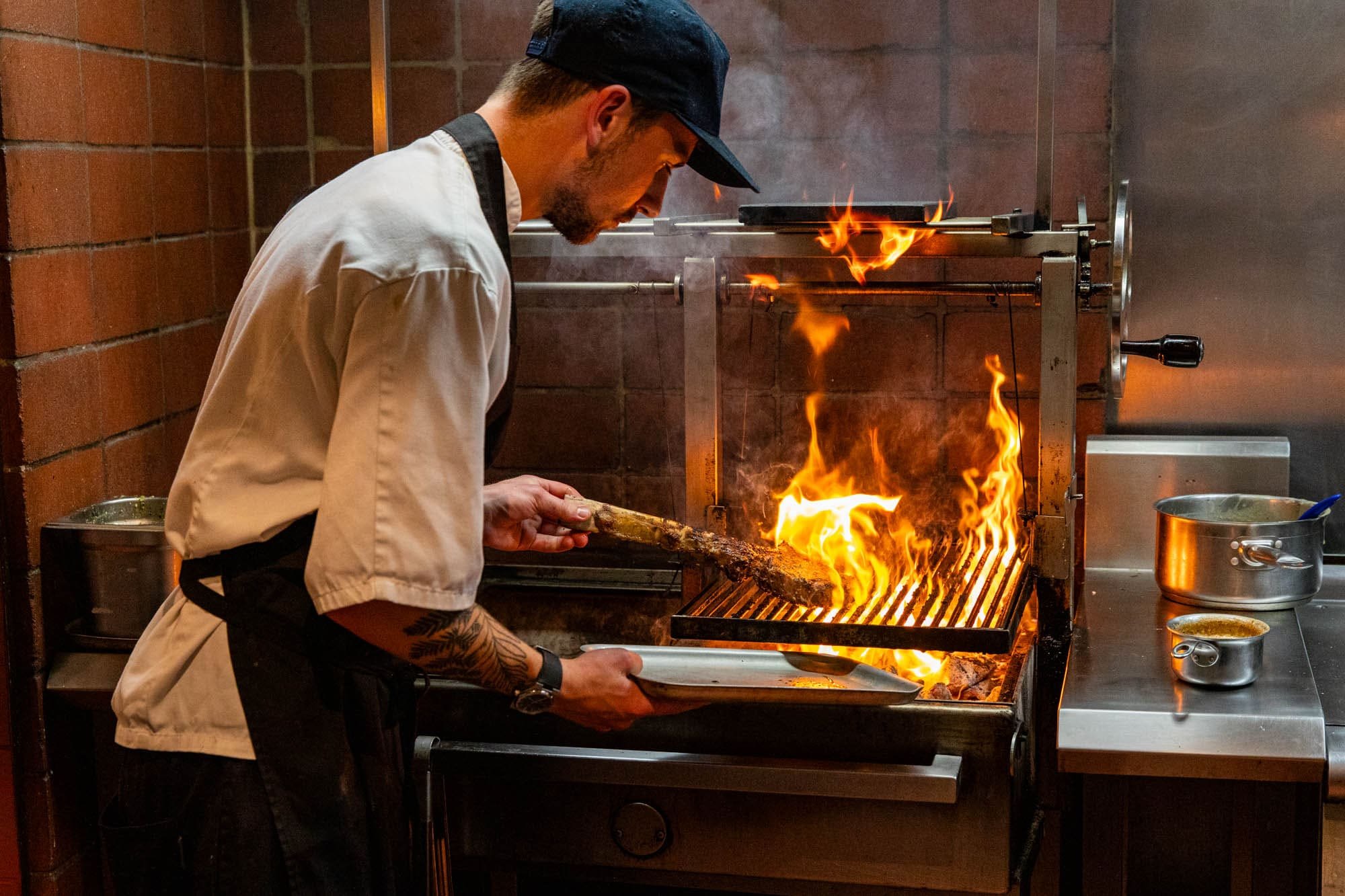 Chef at Kindling open kitchen cooking a Tomahawk steak